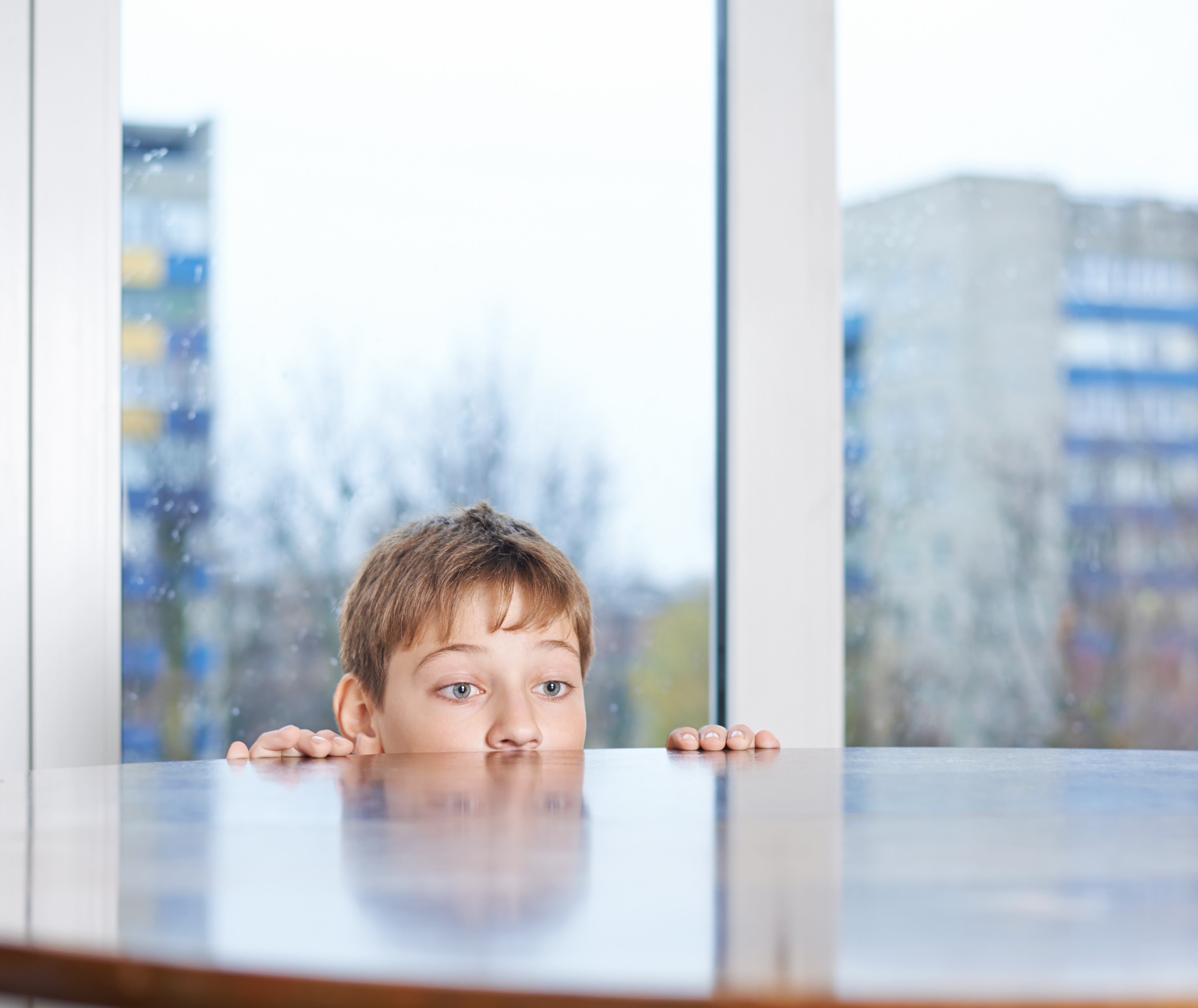 Ein kleiner Junge, der hinter einem Holztisch hervorschaut | Quelle: Shutterstock