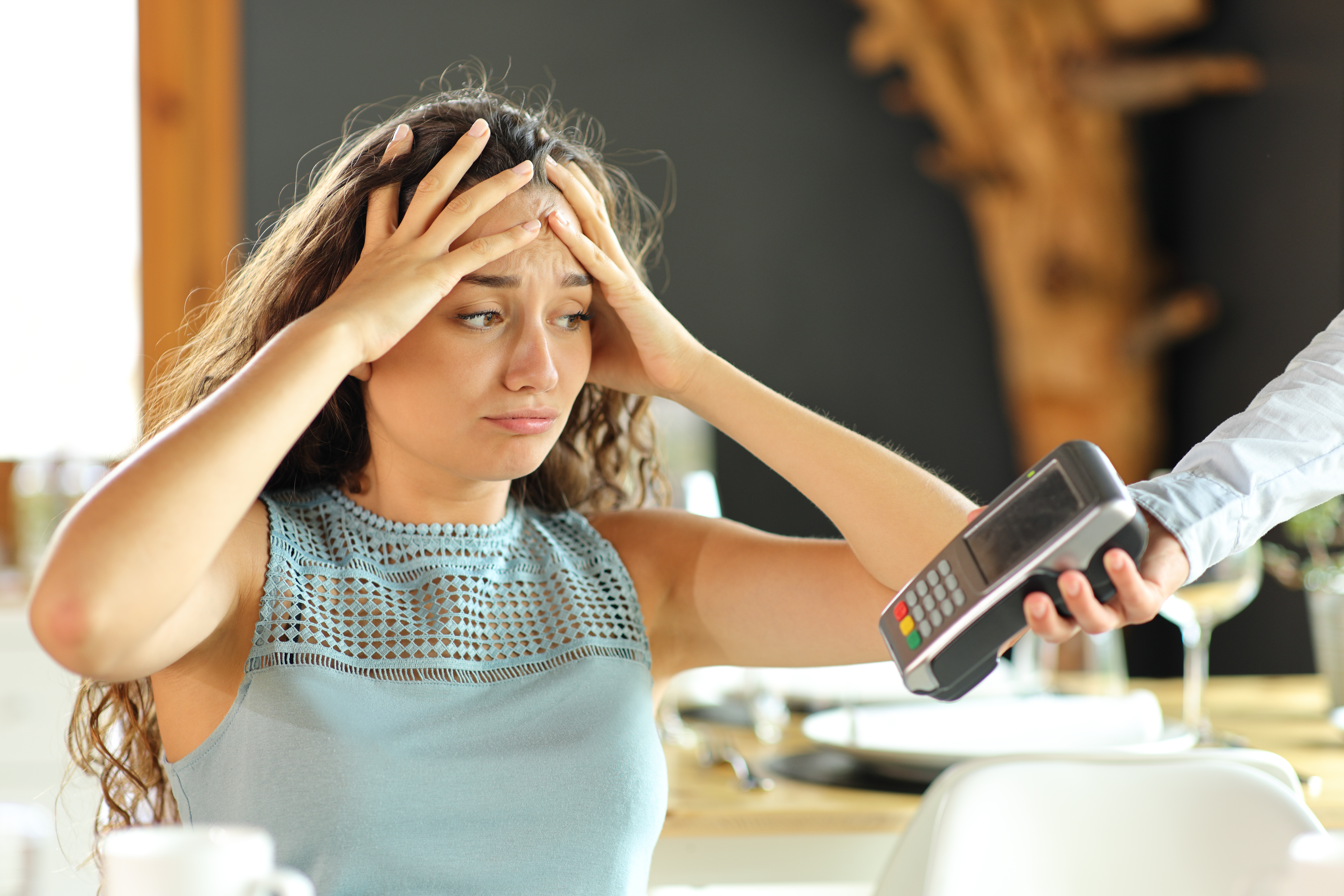 Eine verzweifelt dreinblickende Frau, der eine Kreditkartenmaschine gereicht wird | Quelle: Shutterstock