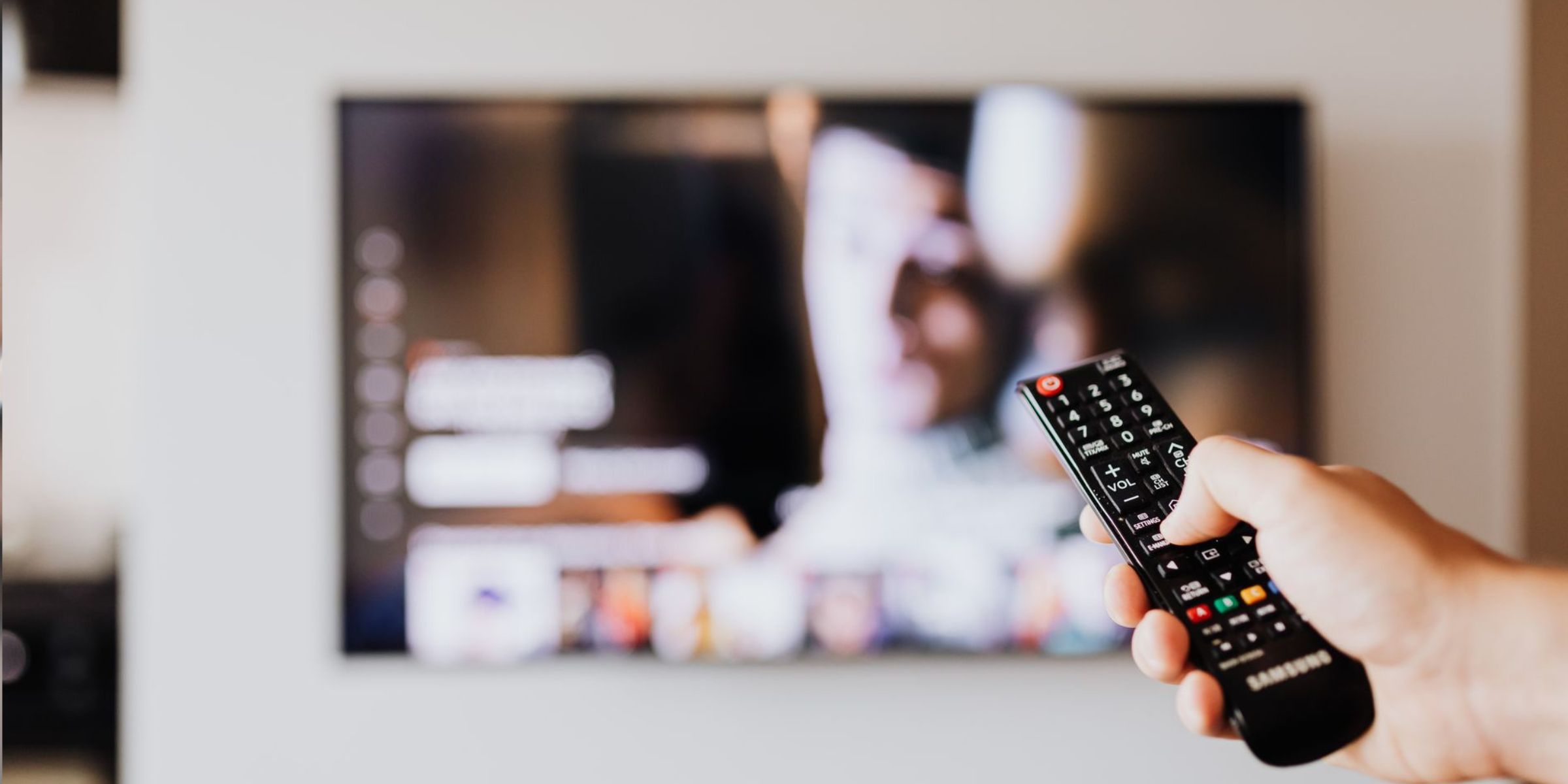Eine Person, die eine Fernbedienung bedient, im Hintergrund ein unscharfer Fernsehbildschirm | Quelle: Pexels