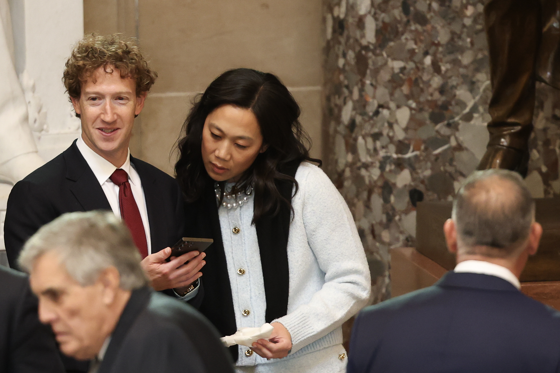 Priscilla Chan schaut auf Mark Zuckerbergs Telefon, während sie bei der Amtseinführung von Donald Trump nebeneinander stehen. | Quelle: Getty Images