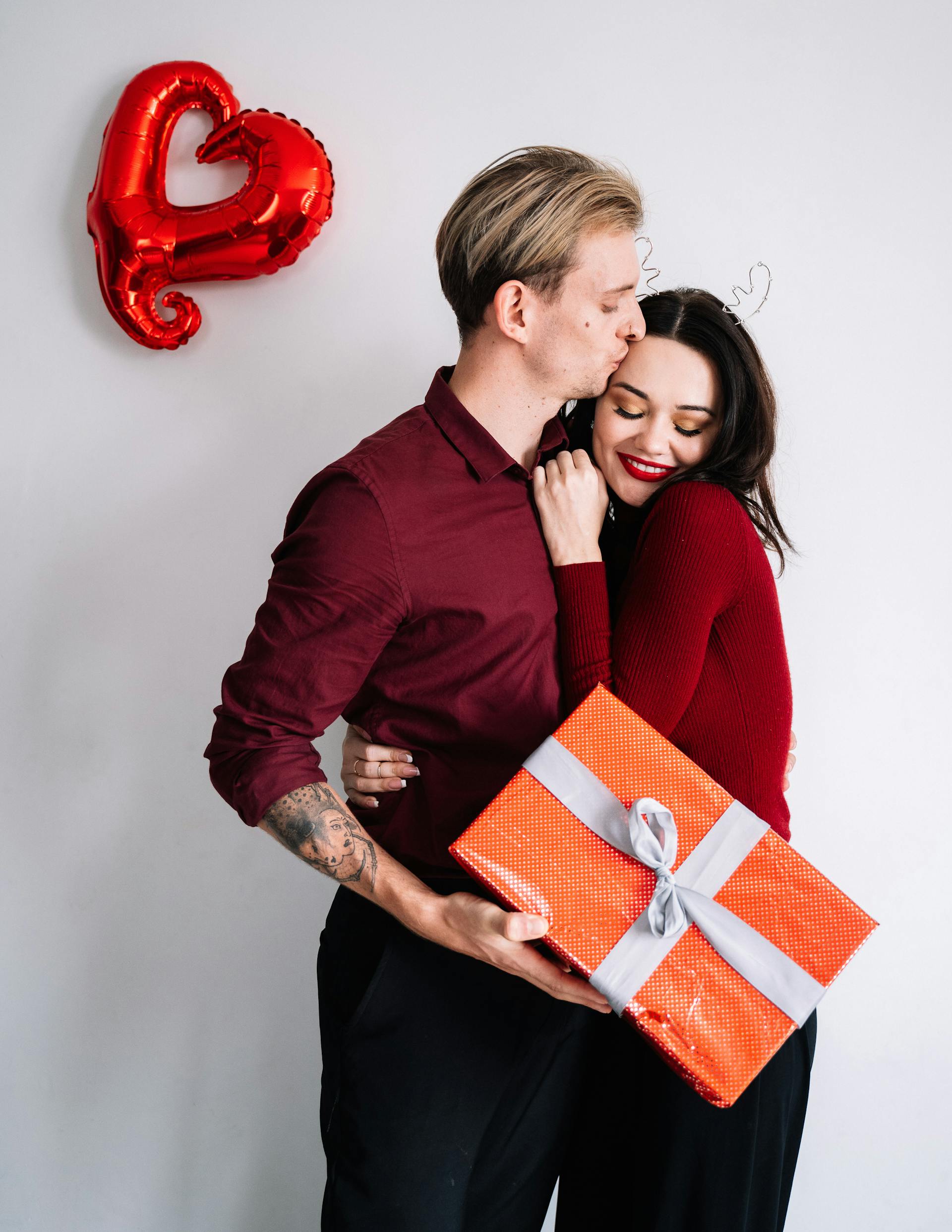 Ein Mann küsst eine Frau, während er eine Geschenkbox hält | Quelle: Pexels