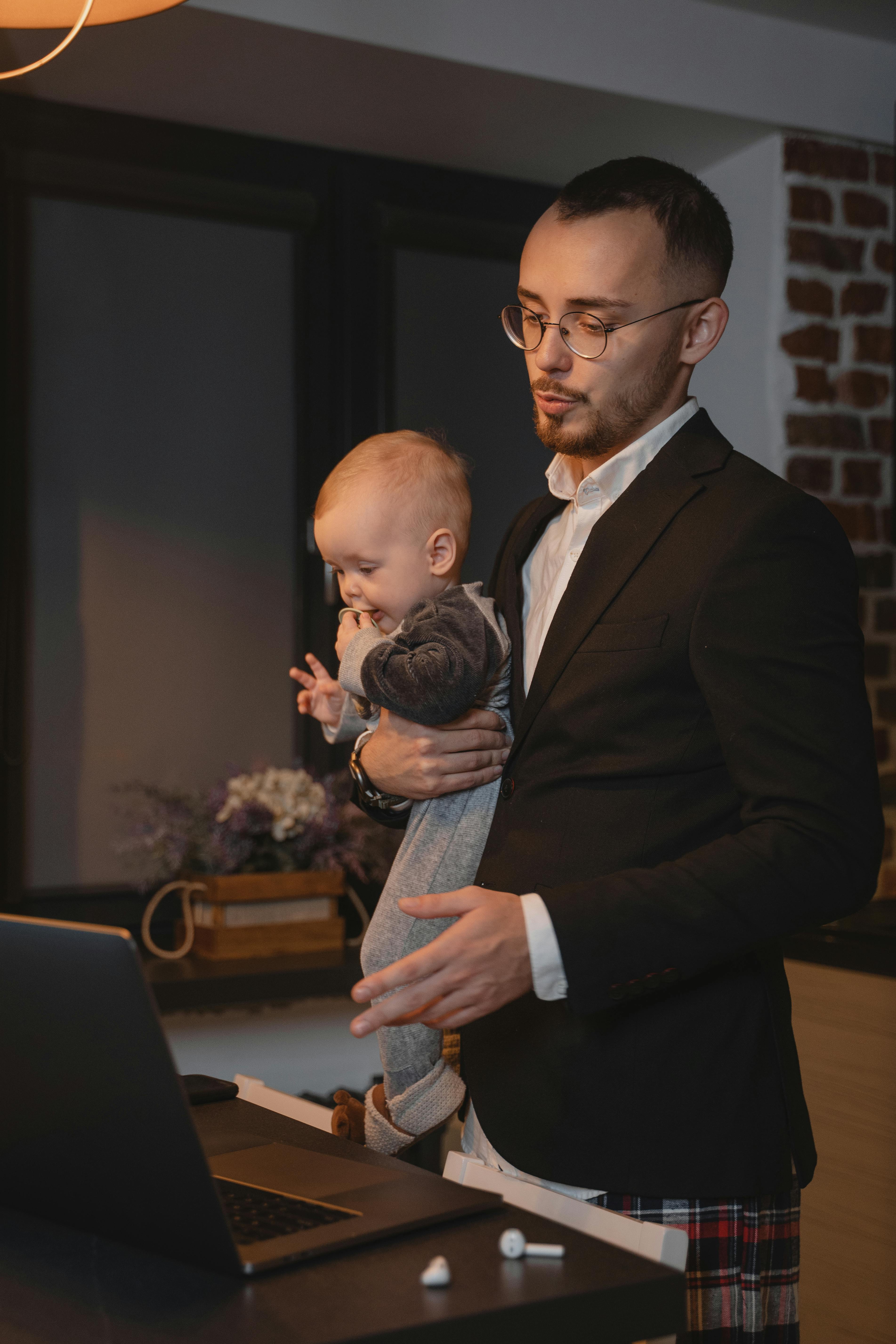Ein Vater trägt ein Baby, während er an seinem Laptop sitzt | Quelle: Pexels