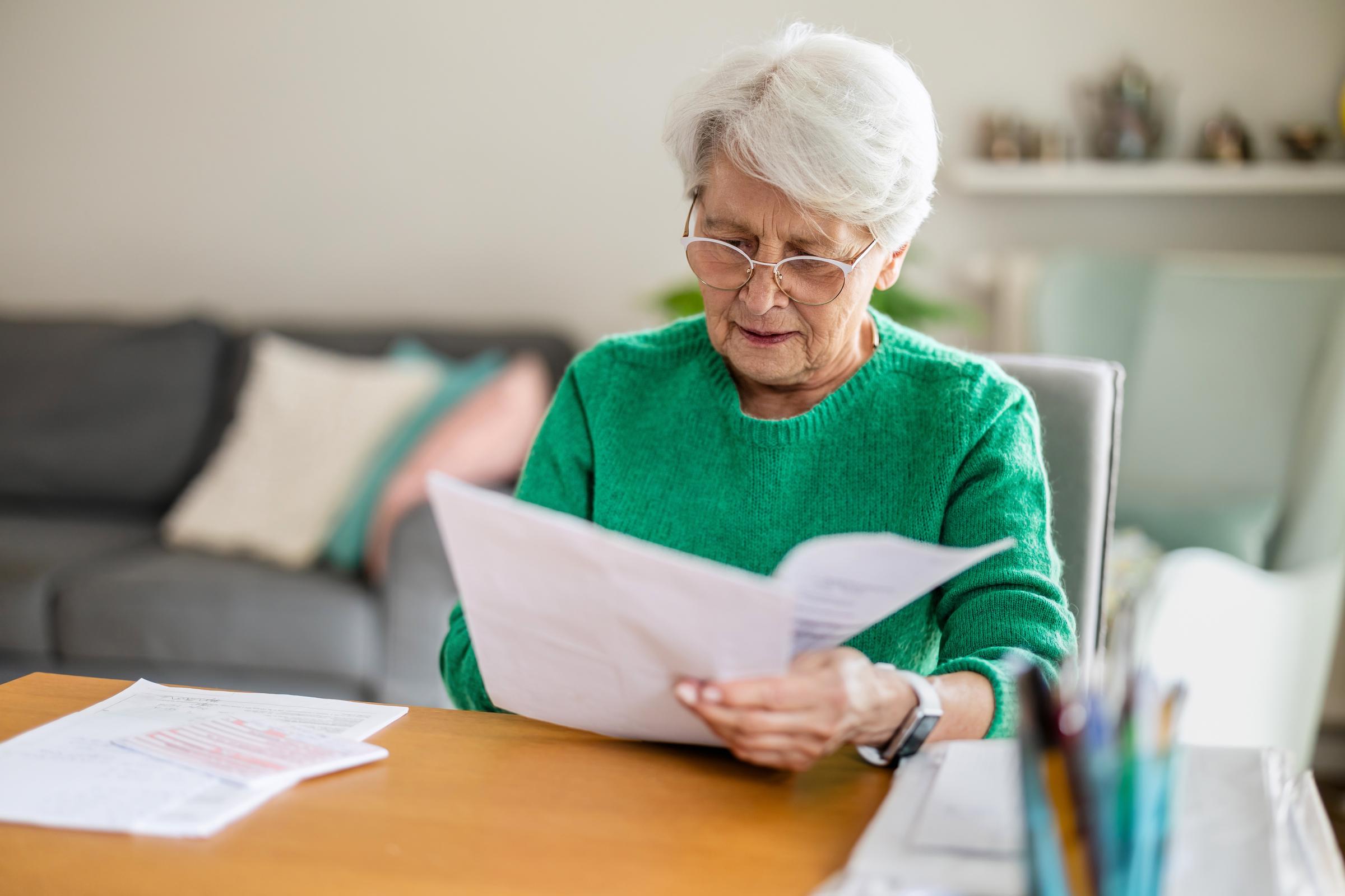 Ältere Frau sitzt im Wohnzimmer und erledigt Papierkram | Quelle: Shutterstock
