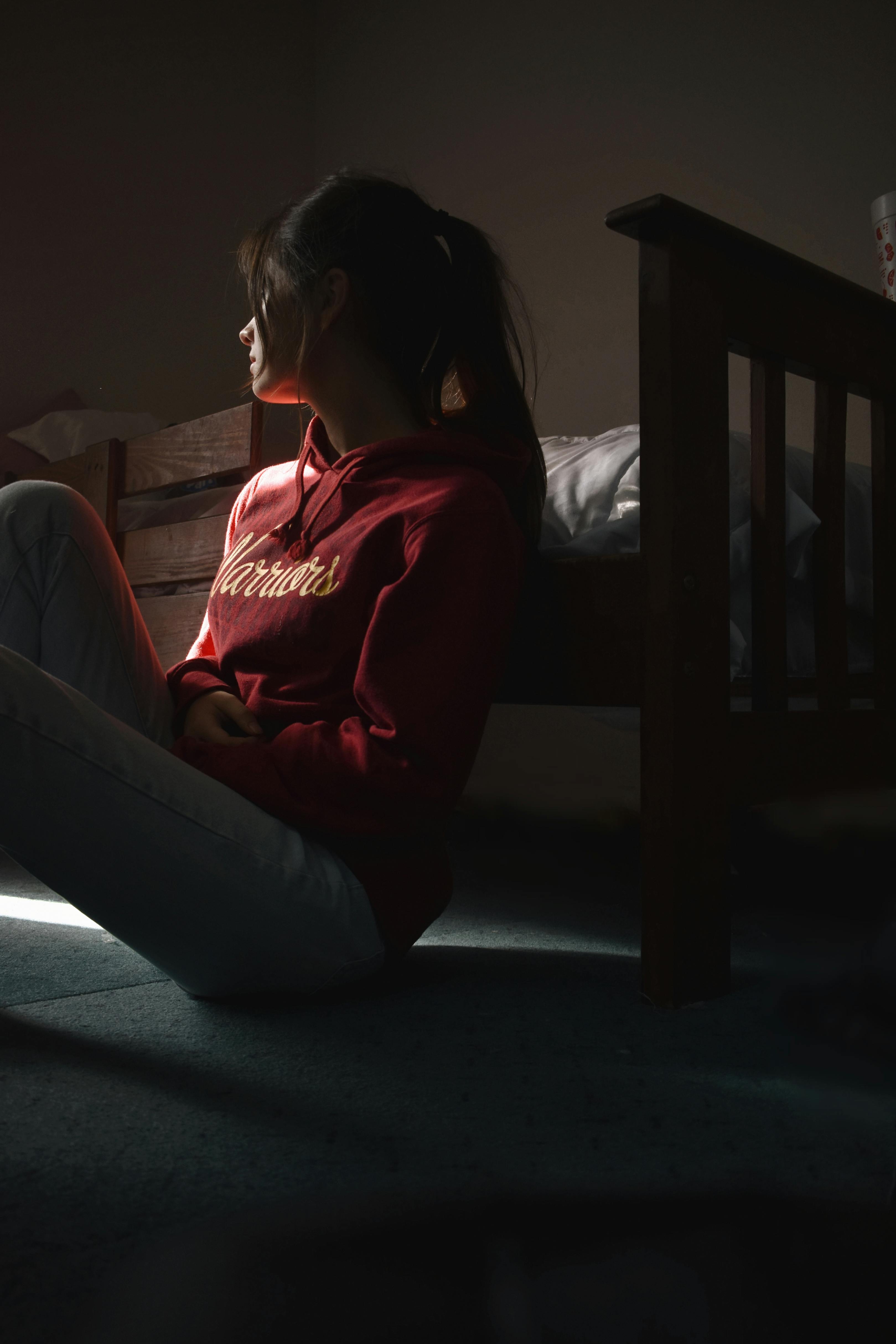 Ein Teil der Silhouette einer traurigen Frau, die neben ihrem Bett auf dem Boden sitzt | Quelle: Pexels