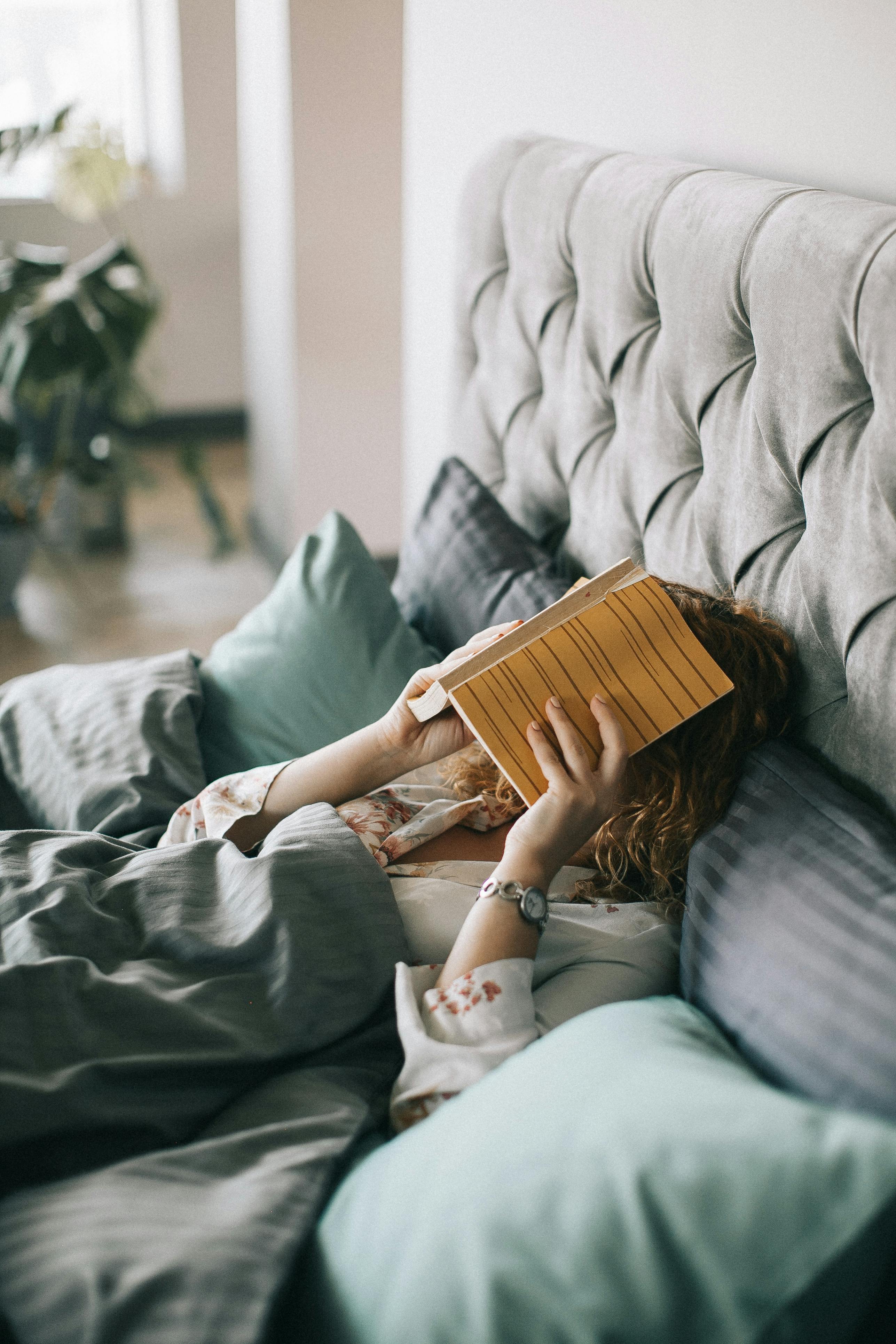 Eine Frau, die im Bett liegt und ihr Gesicht mit einem Buch bedeckt | Quelle: Pexels