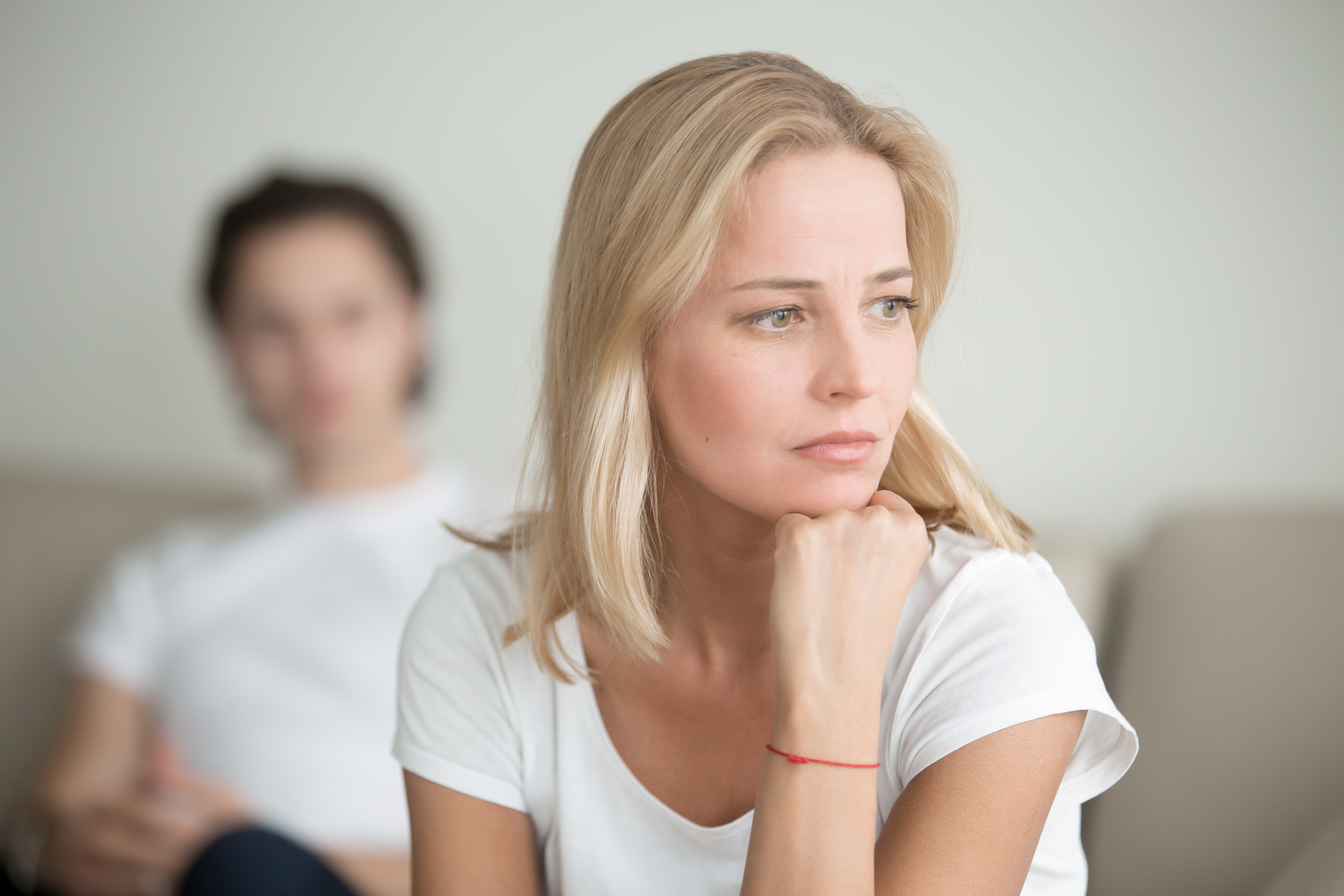 Eine Frau, die tief in Gedanken versunken ist, während ein anderer Mann sie von hinten beobachtet | Quelle: Shutterstock