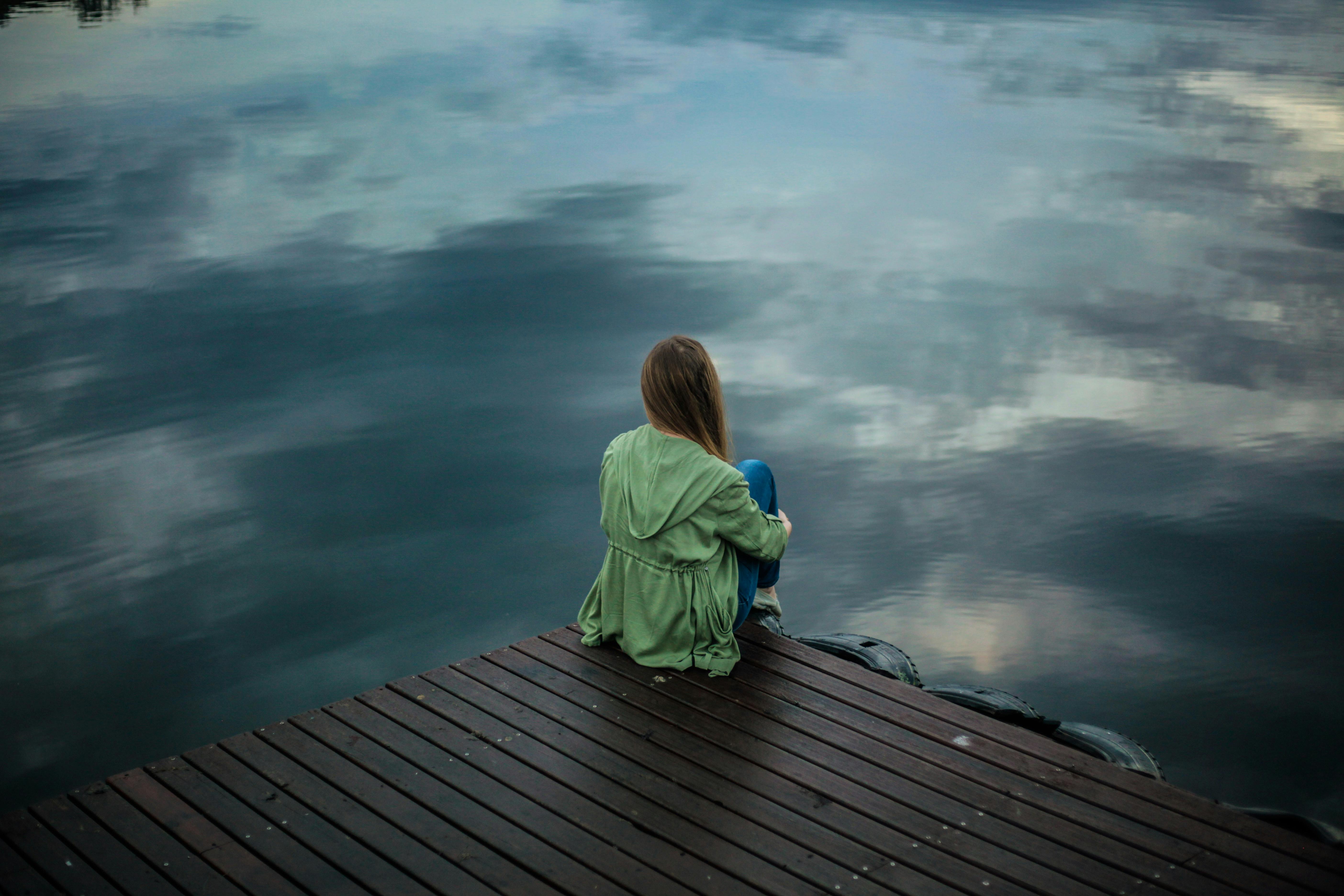 Eine Frau, die alleine auf einem Steg sitzt | Quelle: Pexels