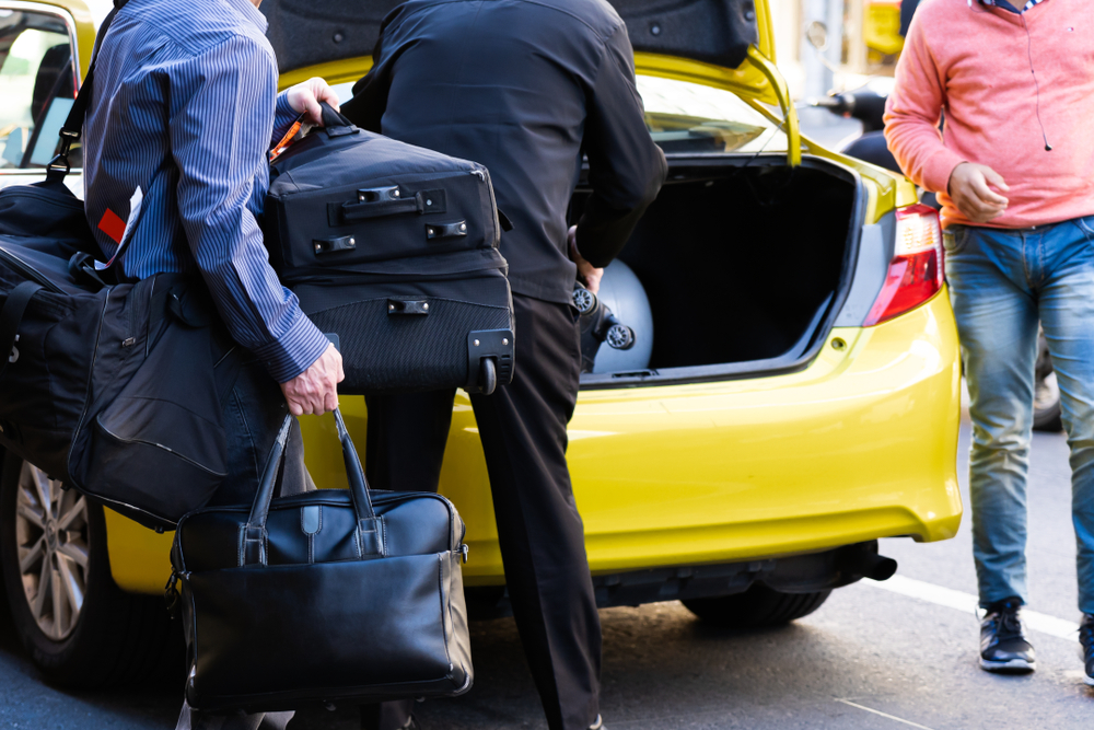 Fahrgäste laden ihr Gepäck in den Kofferraum des Taxis. | Quelle: Shutterstock