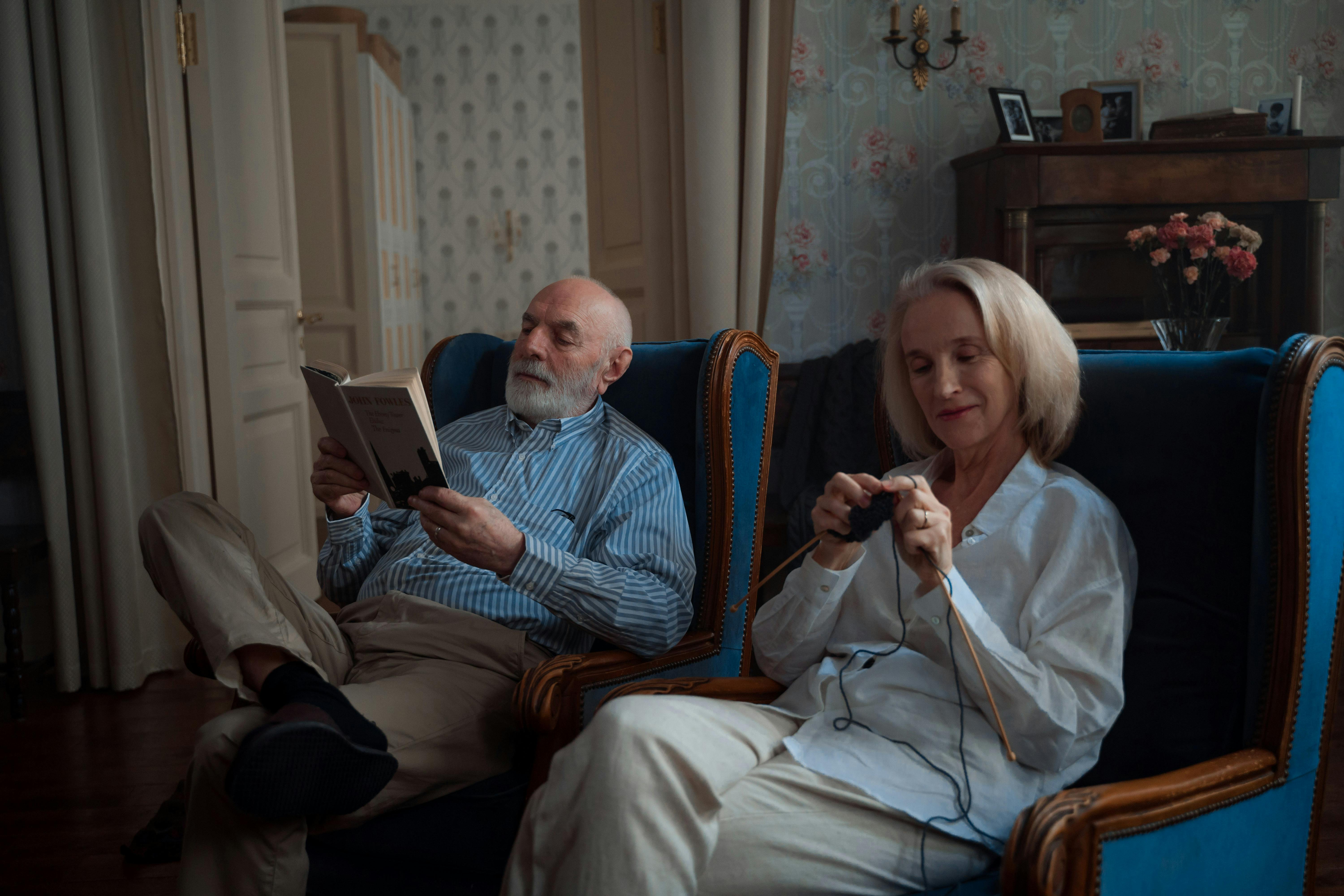 Ein Mann liest ein Buch, während seine Frau fröhlich strickt | Quelle: Pexels