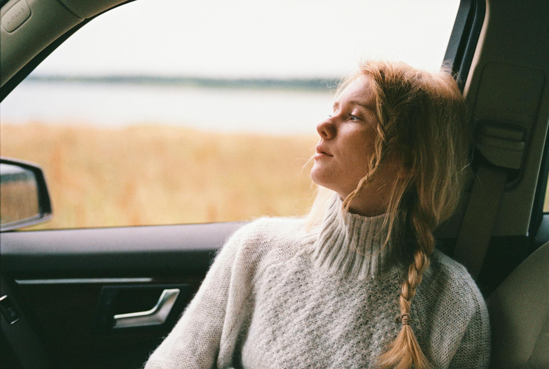 Eine Frau im Pullover sitzt in einem Auto und denkt nach | Quelle: Pexels