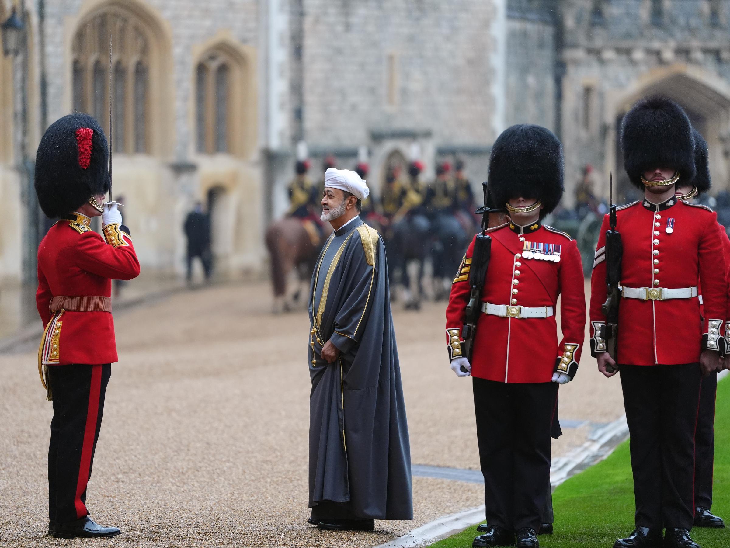 Sultan Haitham bin Tarik von Oman nimmt am 20. Oktober 2026 während der feierlichen Begrüßung auf dem Innenhof von Windsor Castle in Windsor, England, die Ehrenwache ab. Der Gastmonarch trägt einen knöchellangen grauen Bisht mit goldbestickten Schultern und Besatz über einem weißen Turban und steht aufmerksam da, während ein Offizier in scharlachroter Uniform und Bärenfellmütze neben Gardisten in voller Zeremonienuniform mit erhobenem Schwert salutiert. | Quelle: Getty Images