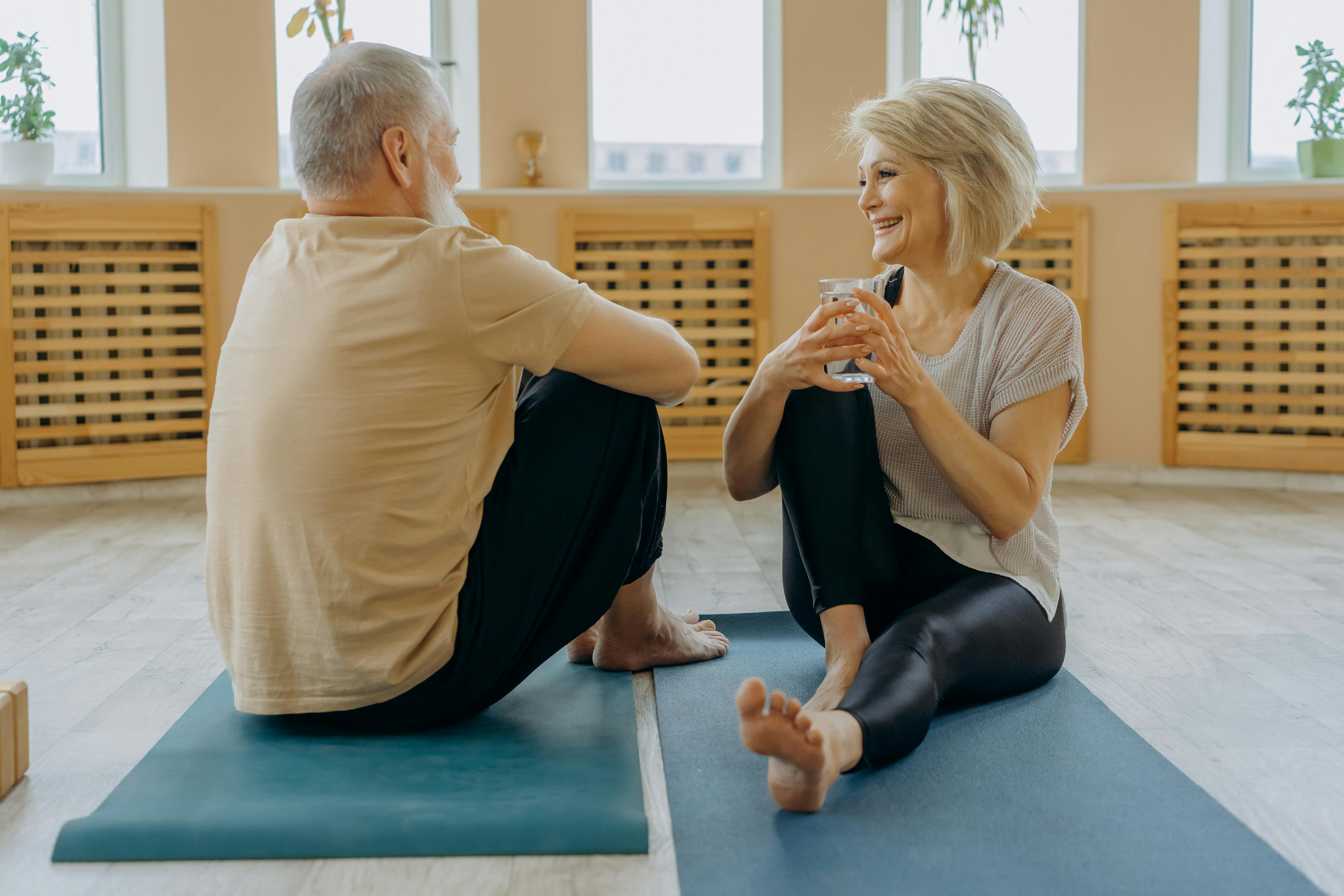 Ein älterer Mann und eine Frau unterhalten sich, während sie auf einer Yogamatte sitzen | Quelle: Pexels