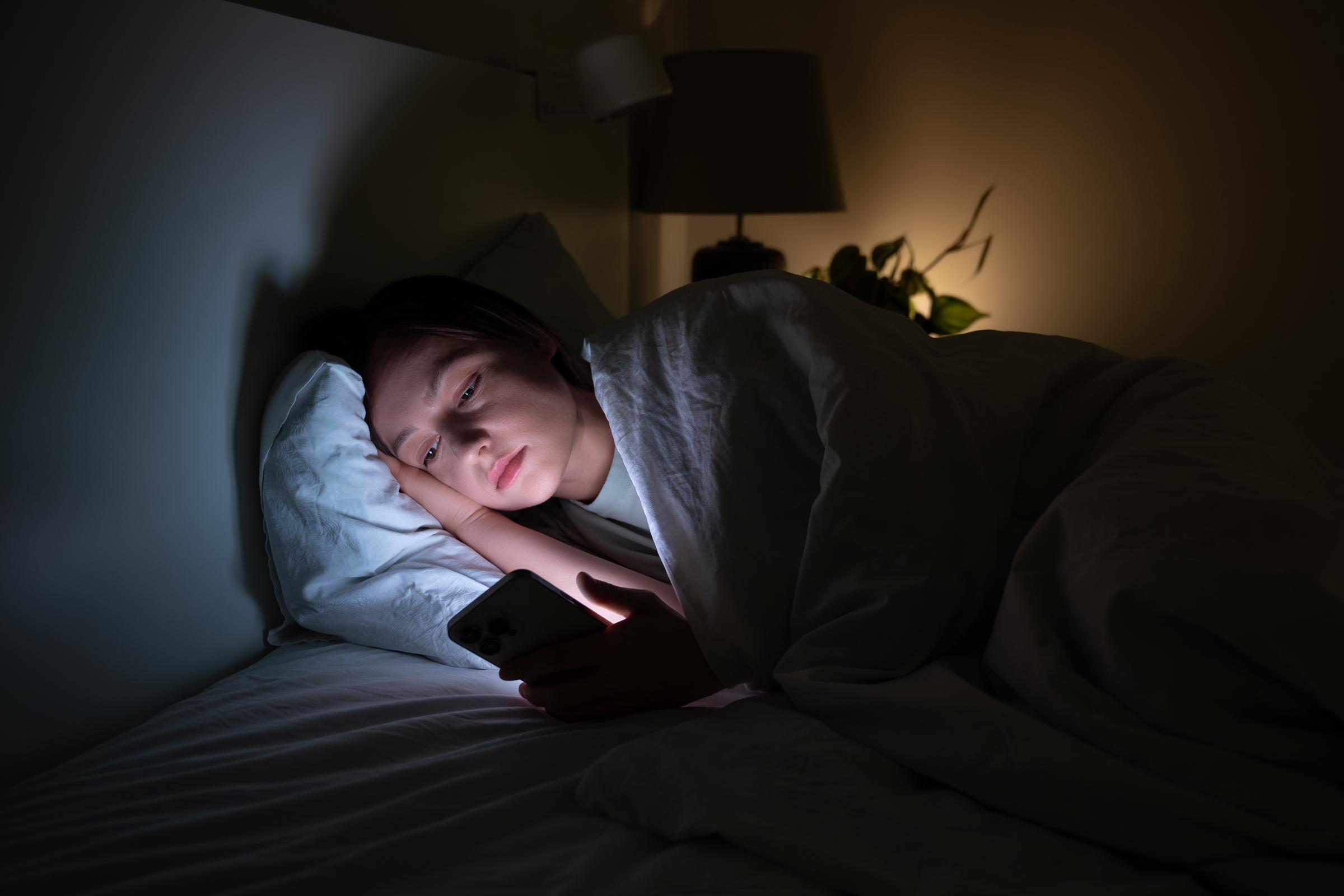 Eine Frau, die im Bett auf ihrem Handy scrollt | Quelle: Getty Images