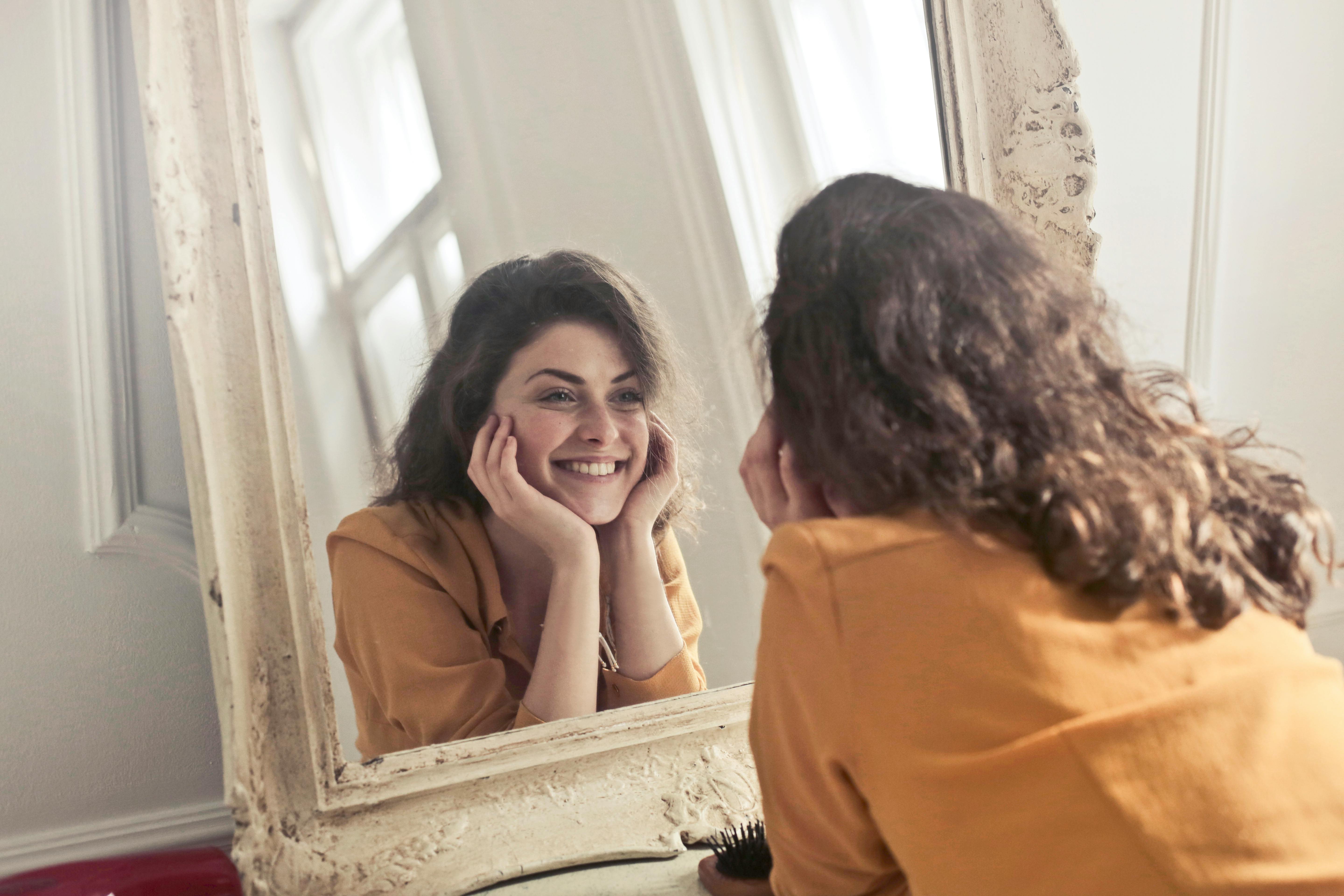 Eine Frau lächelt, während sie ihr Spiegelbild betrachtet | Quelle: Pexels