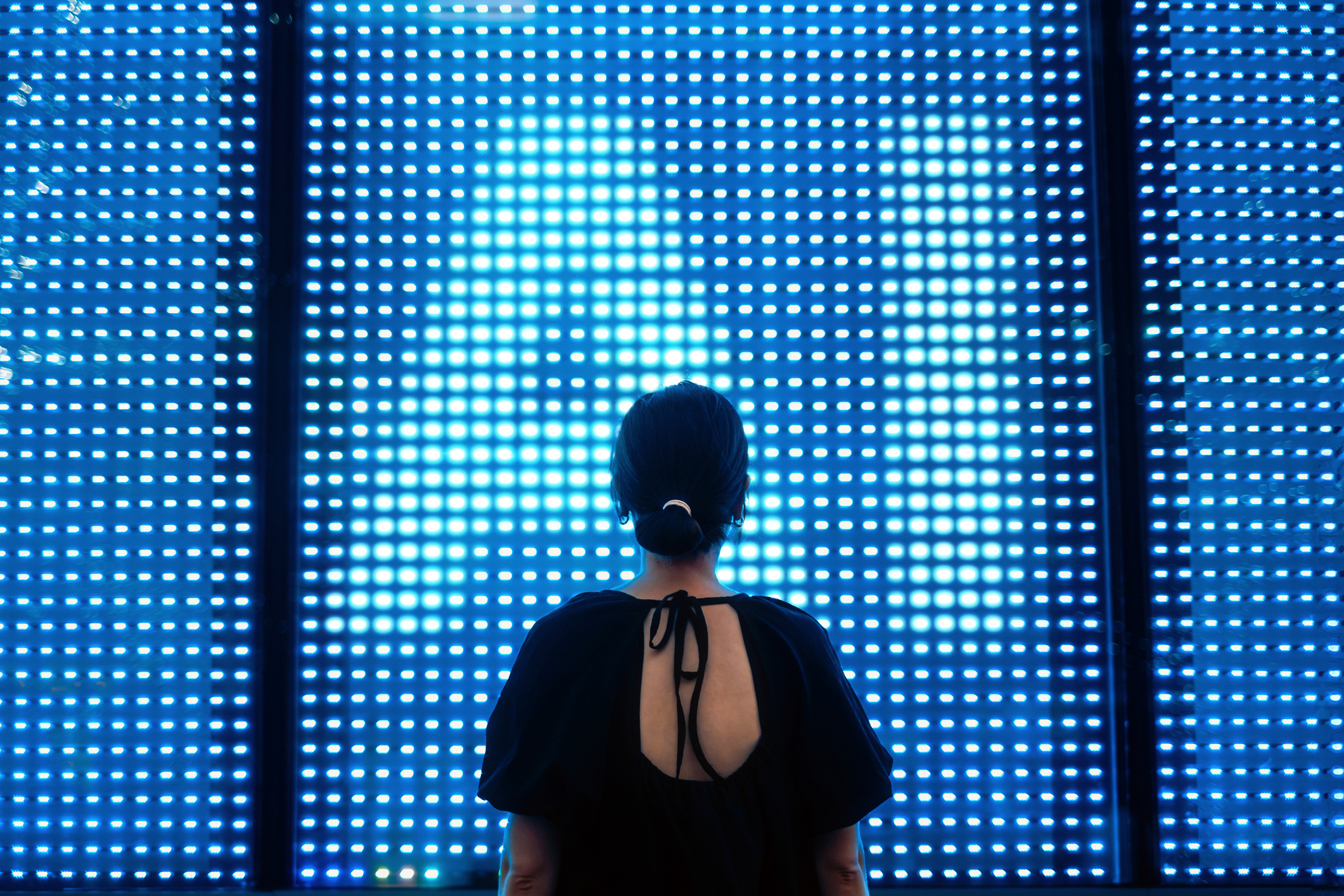 Rückansicht einer jungen asiatischen Geschäftsfrau, die vor einer beleuchteten Digitalanzeige in der Stadt steht und einen Bildschirm mit KI-Technologie nutzt. | Quelle: Getty Images