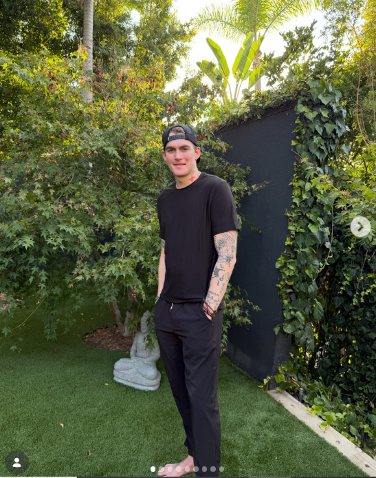 In einem Beitrag vom 5. August 2026 stand der 27-jährige Presley Gerber barfuß auf einem üppig grünen Rasen neben einer Buddha-Statue und viel Grün und präsentierte sich ganz entspannt in einem komplett schwarzen Freizeit-Outfit, bestehend aus einem T-Shirt mit Rundhalsausschnitt, einer passenden Hose, einer verkehrt herum getragenen Baseballkappe und Perlenarmbändern, die seine Tattoos an Ärmel und Hals besonders zur Geltung brachten. | Quelle: Instagram/presleygerber
