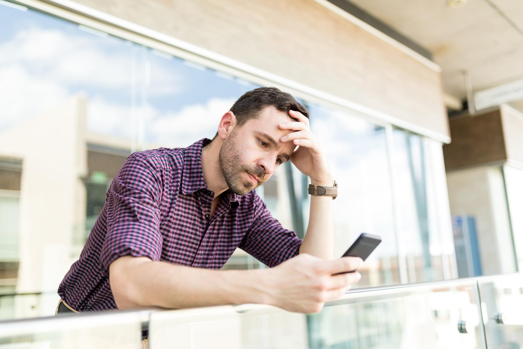 Ein aufgebrachter Mann, der auf einem Balkon steht und auf sein Telefon schaut | Quelle: Freepik