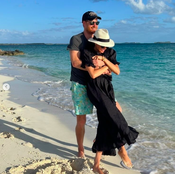 Prinz Harry umarmt Meghan Markle liebevoll, während die beiden lächelnd für ein Foto am Strand posieren. | Quelle: Instagram/meghan