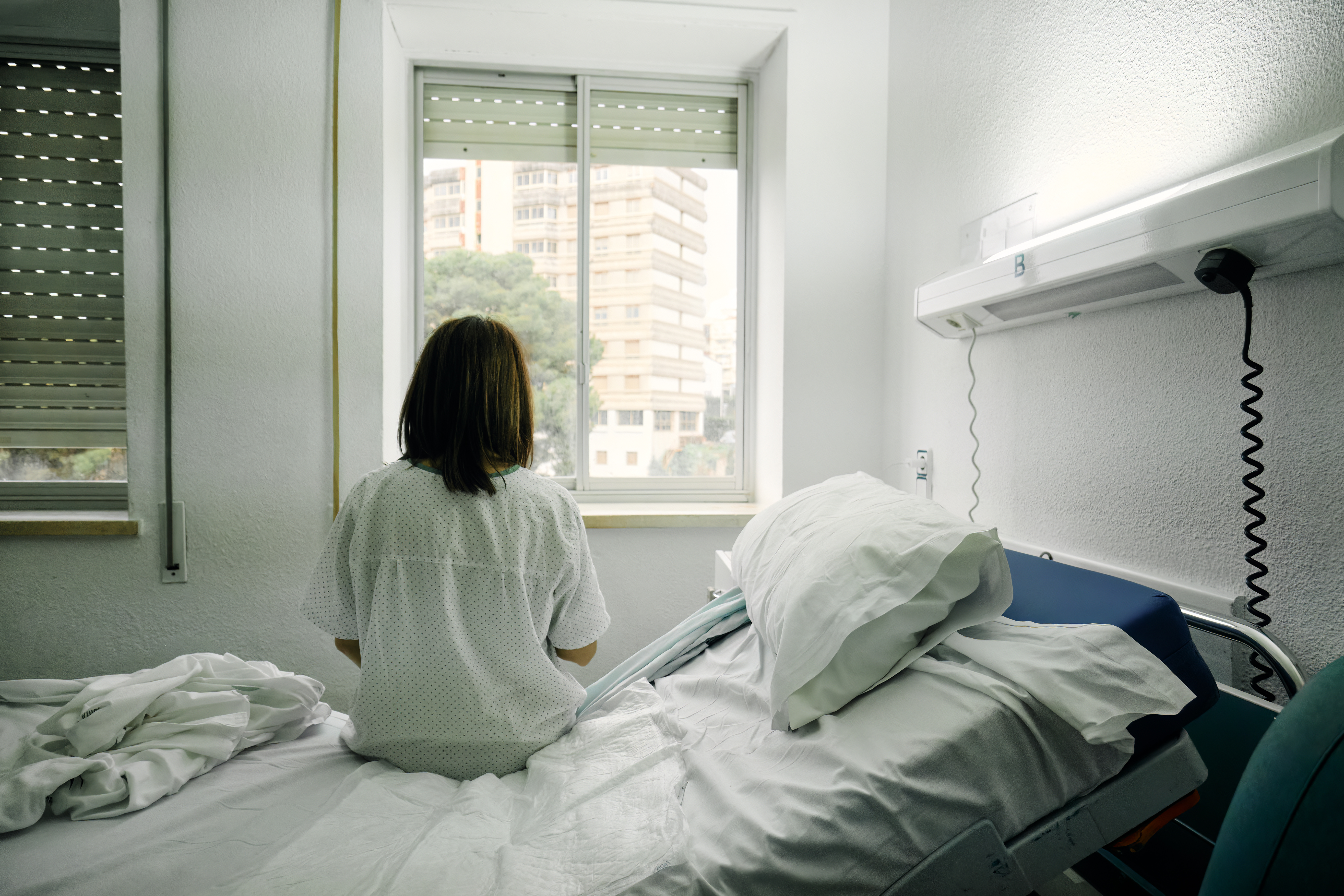 Rückenansicht einer Frau, die auf einem Krankenhausbett sitzt | Quelle: Getty Images