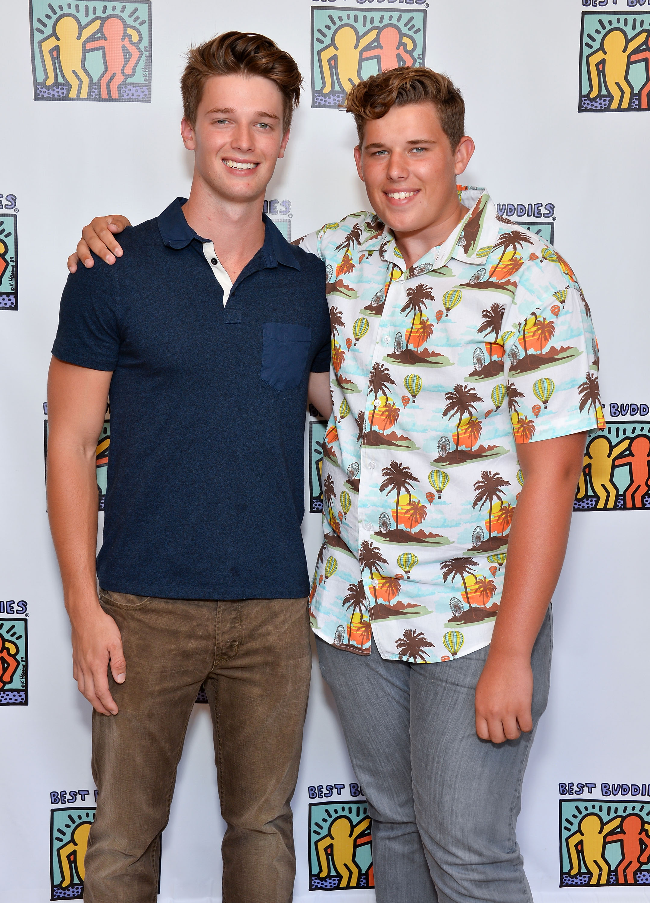 Patrick posiert mit seinem jüngeren Bruder Christopher bei der Team Maria Benefizveranstaltung für Best Buddies in Beverly Hills. Patrick trägt ein navyfarbenes Hemd mit Kragen und braune Jeans, während Christopher in einem farbenfrohen Button-down mit tropischem Aufdruck und einer grauen Hose auffällt und selbstbewusst in die Kamera lächelt.