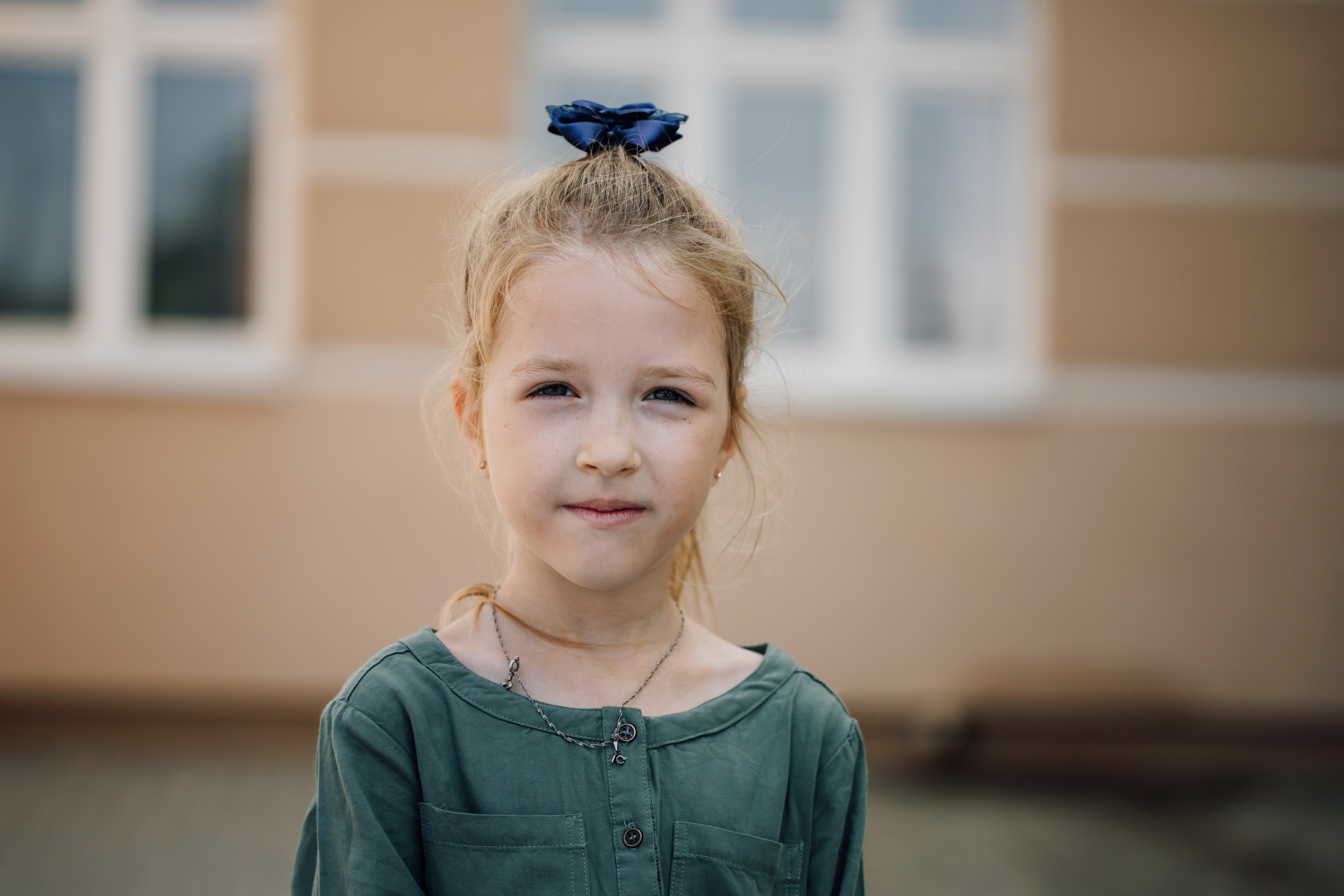 Porträt eines ernsten kleinen Mädchens, das in die Kamera schaut, mit einem Grundschulgebäude im Hintergrund | Quelle: Getty Images
