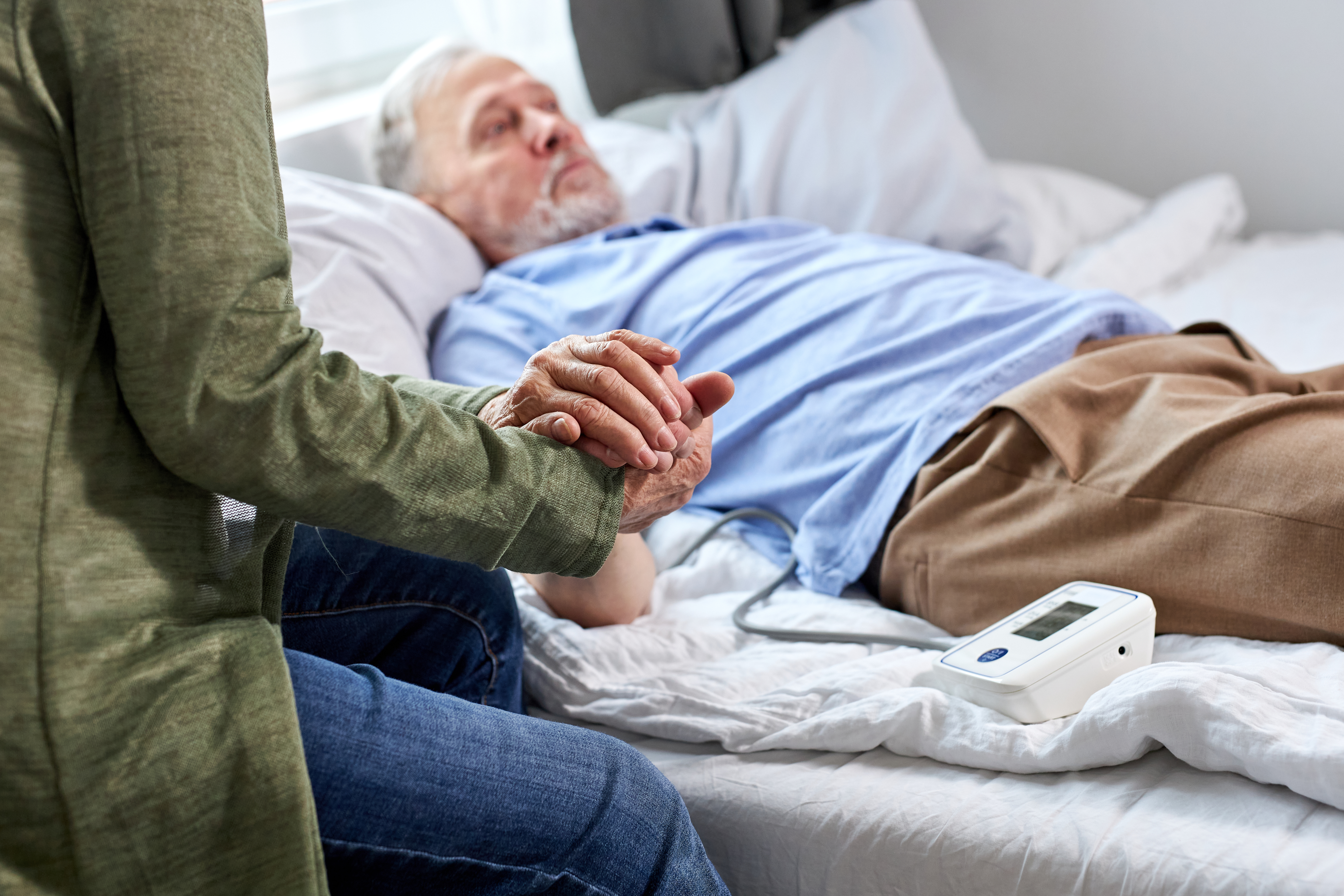 Eine Frau hält die Hand eines kranken älteren Mannes, während sie neben ihm sitzt | Quelle: Shutterstock