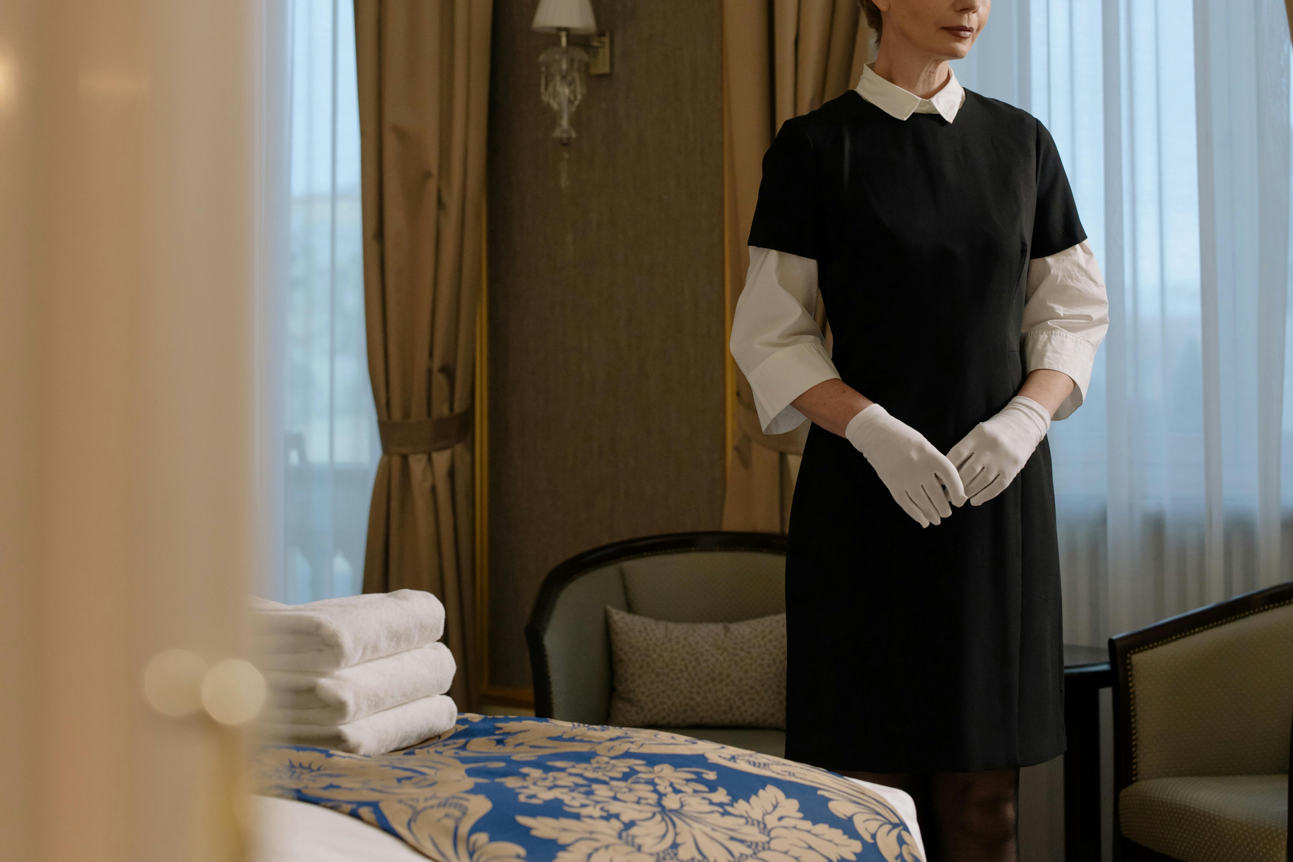 Frau in Uniform neben dem Bett eines Hotelzimmers | Quelle: Pexels