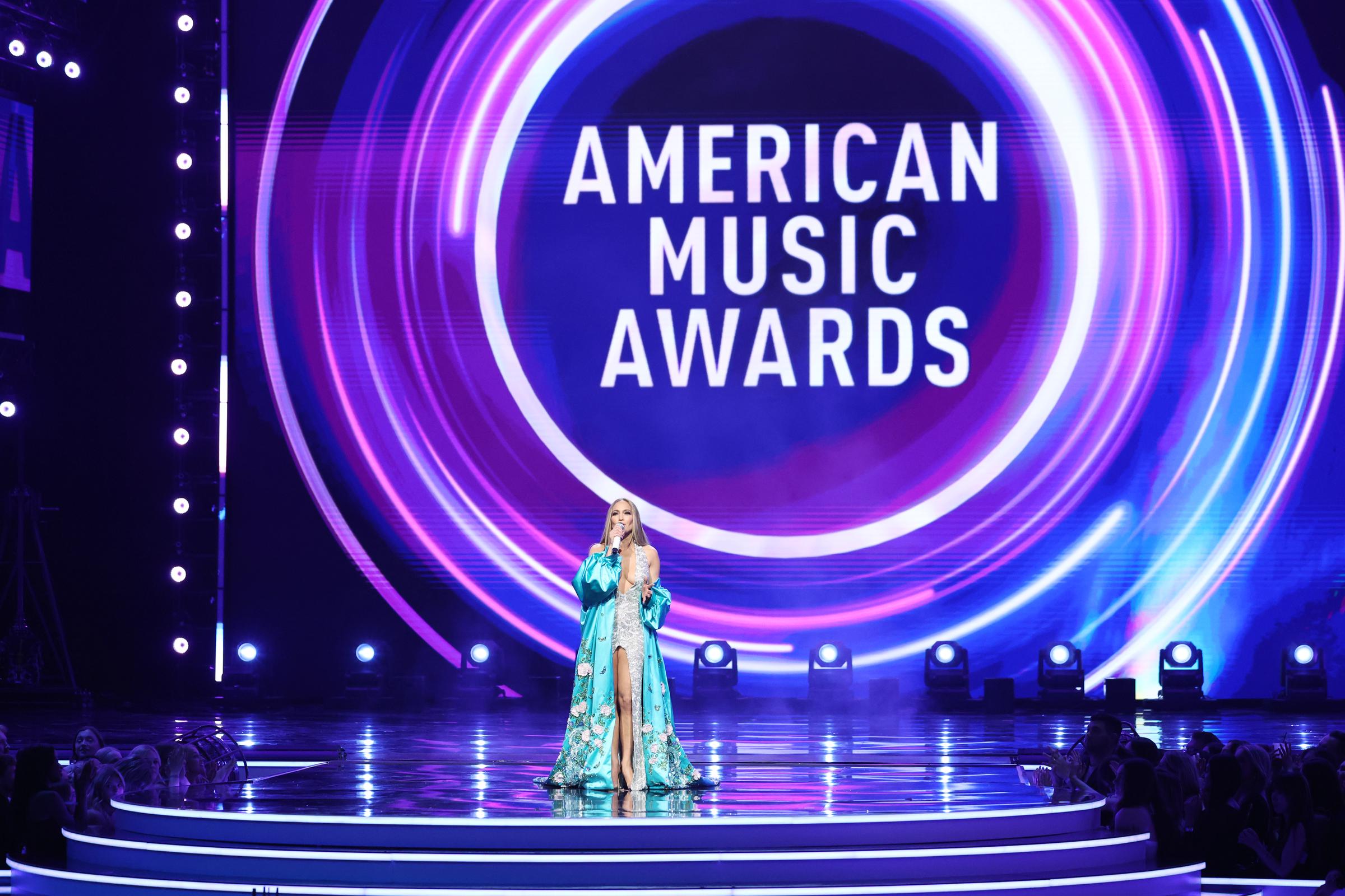 In einem leuchtenden Wirbel aus Rosa und Blau beendet Jennifer Lopez ihren Auftritt bei den American Music Awards, während sie unter dem überragenden Logo der Veranstaltung steht.