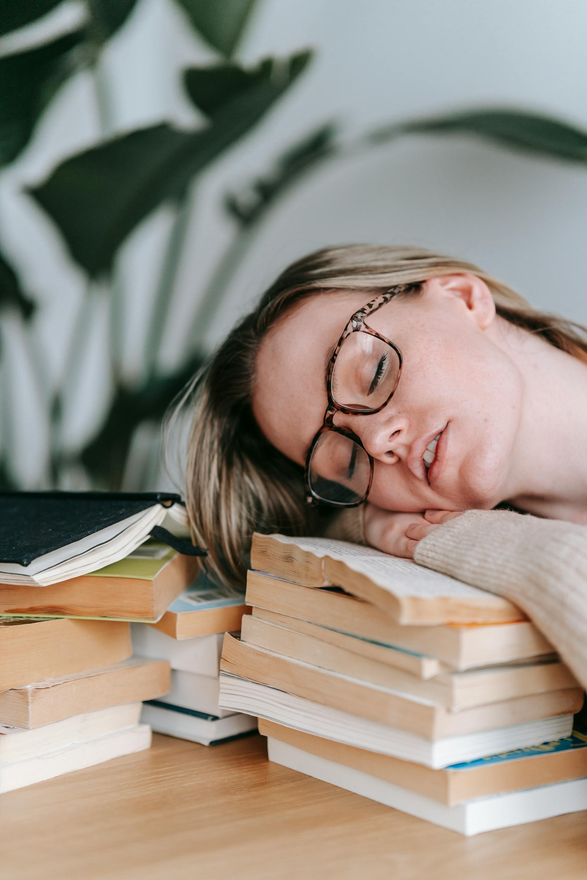 Eine müde junge Frau, die ihren Kopf auf einem Bücherstapel ausruht | Quelle: Pexels