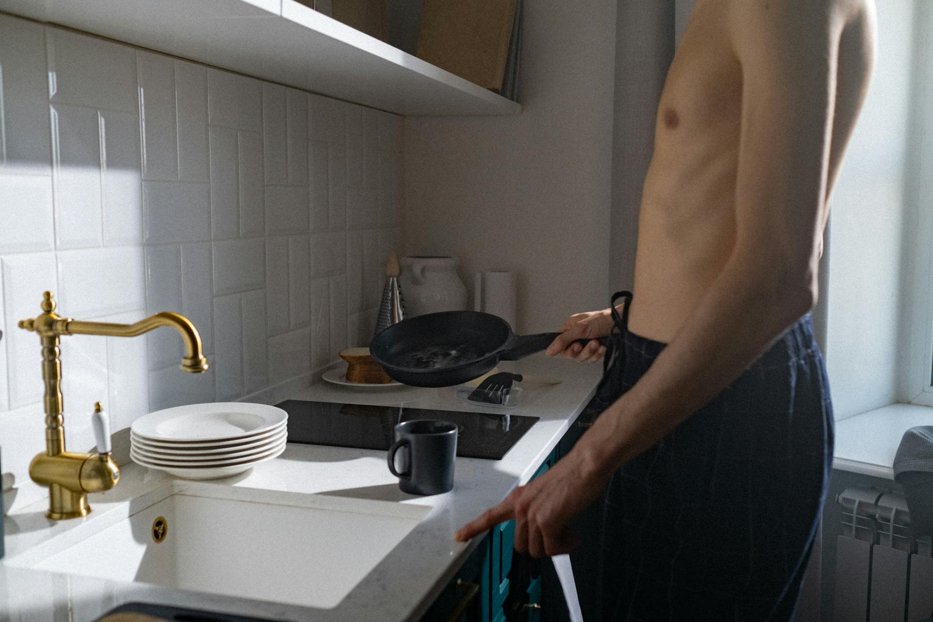 Ein Mann ohne Hemd, der in der Nähe einer Küchenspüle steht | Quelle: Pexels