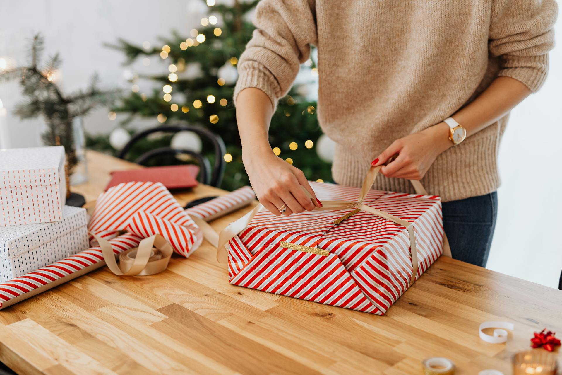 Eine Frau packt ein Geschenk ein, mit einem Weihnachtsbaum im Hintergrund | Quelle: Pexels