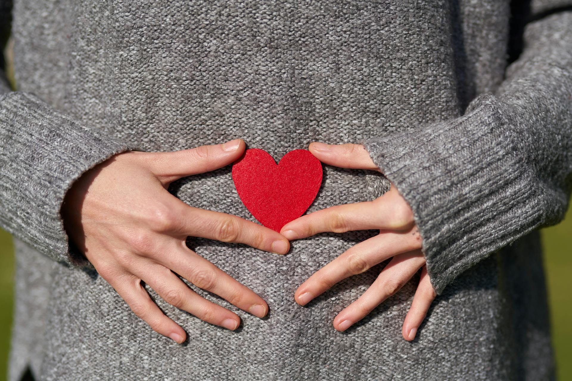 Eine Frau, die einen herzförmigen Ausschnitt in der Nähe ihres Bauches hält | Quelle: Pexels