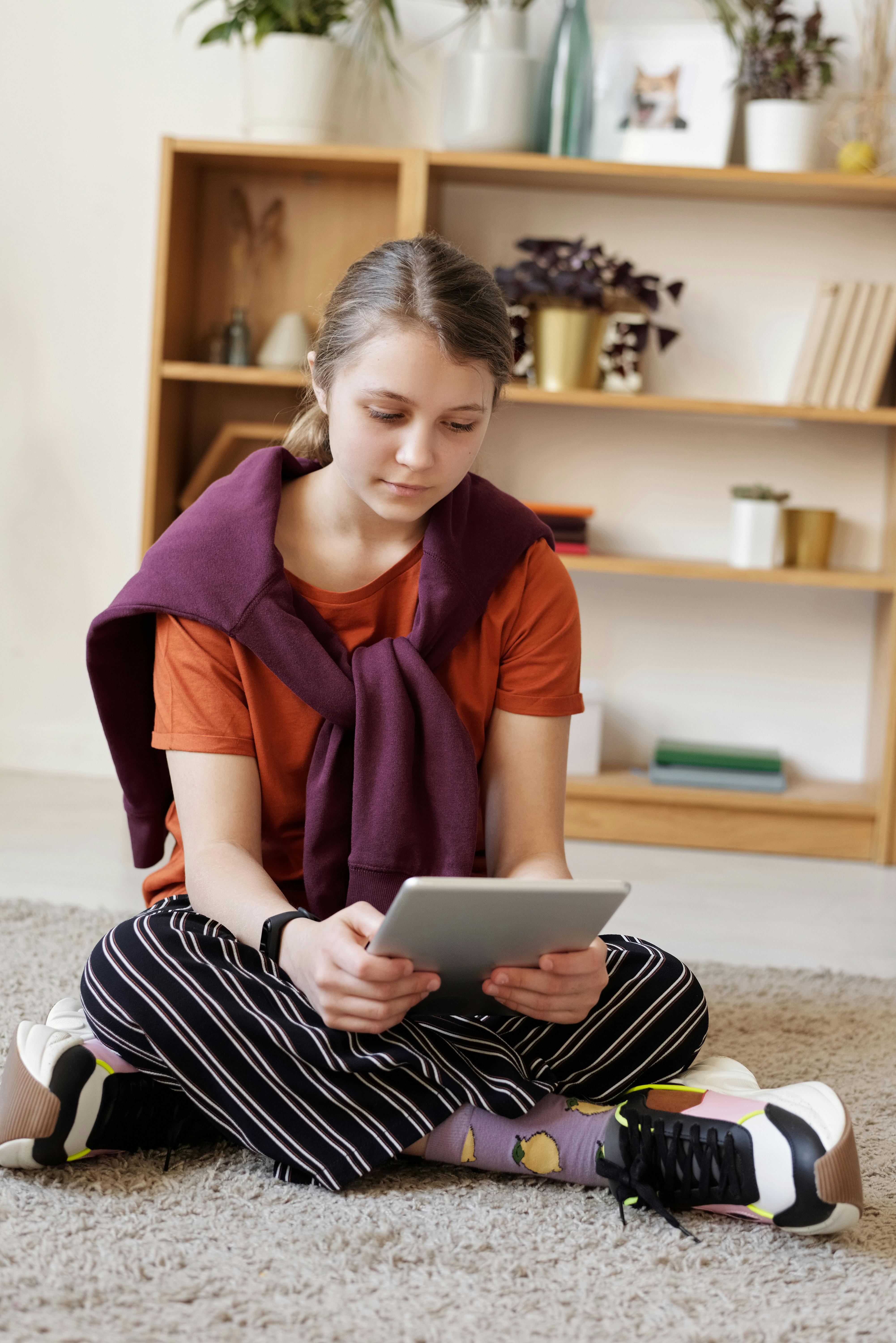 Ein Mädchen im Teenageralter sitzt auf dem Boden und benutzt ein Tablet | Quelle: Pexels