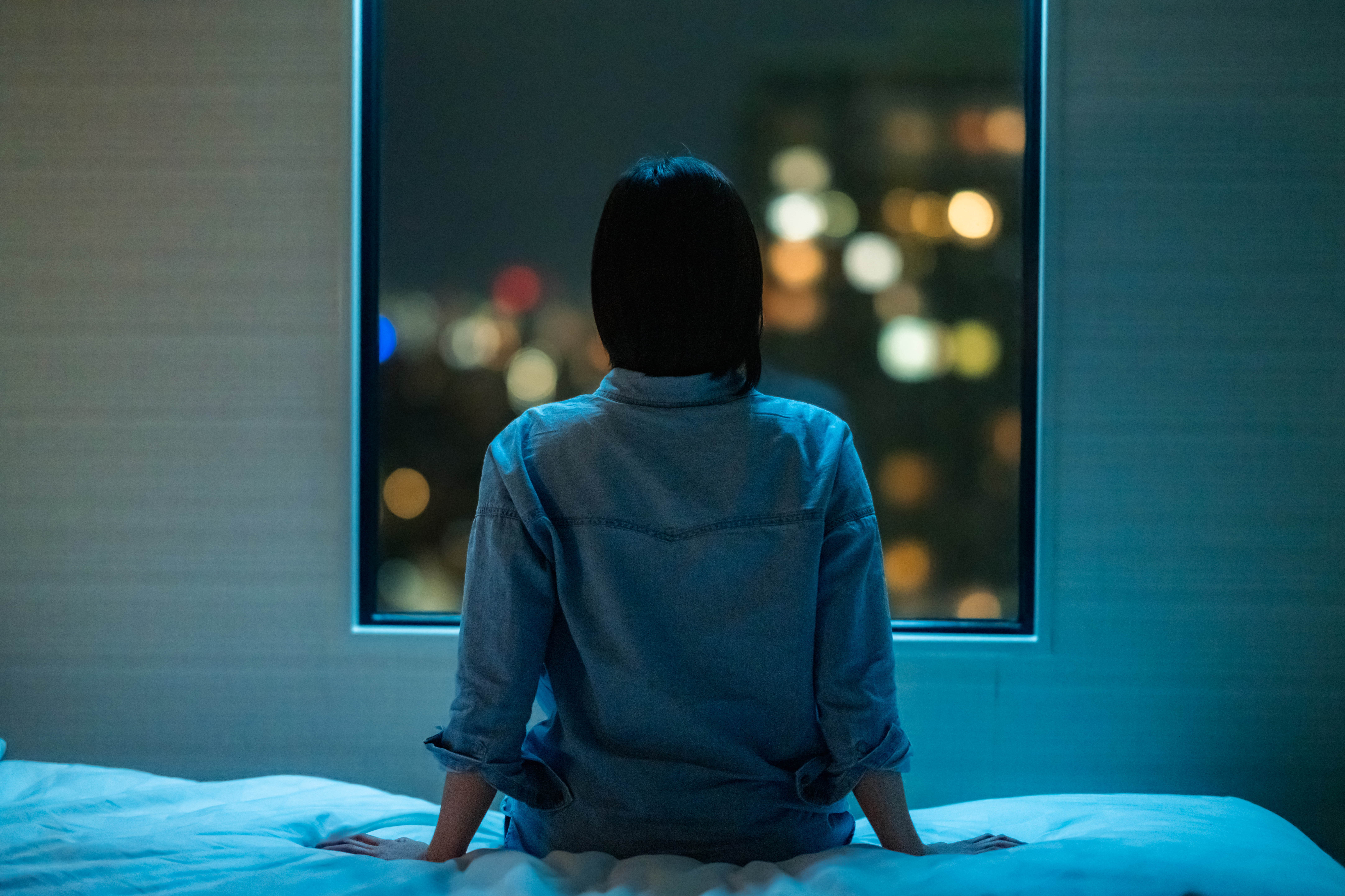 Rückansicht einer Frau, die nachts allein auf dem Bett sitzt und durch das Fenster schaut | Quelle: Getty Images