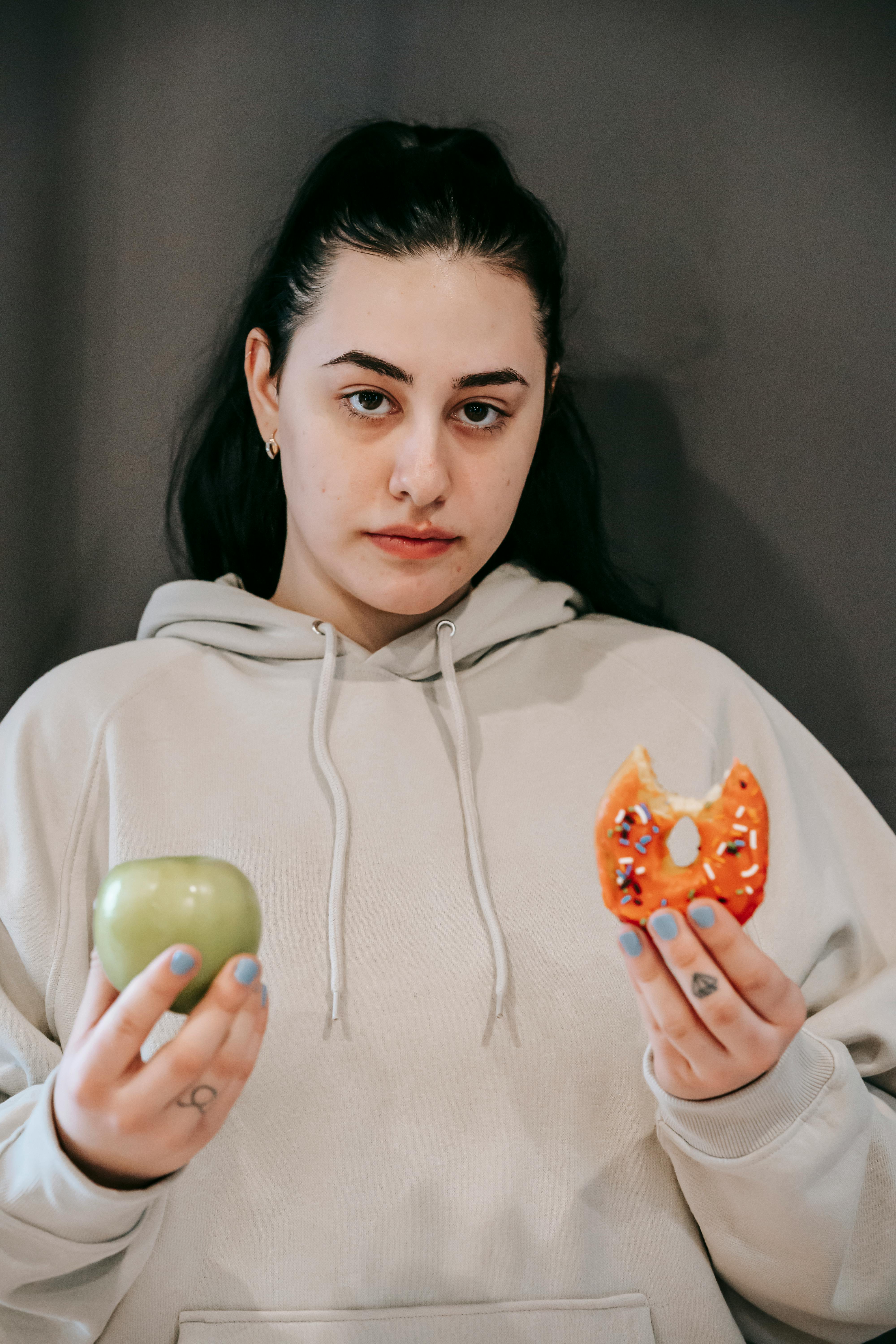 Eine Frau hält einen Apfel und einen Donut in der Hand | Quelle: Pexels