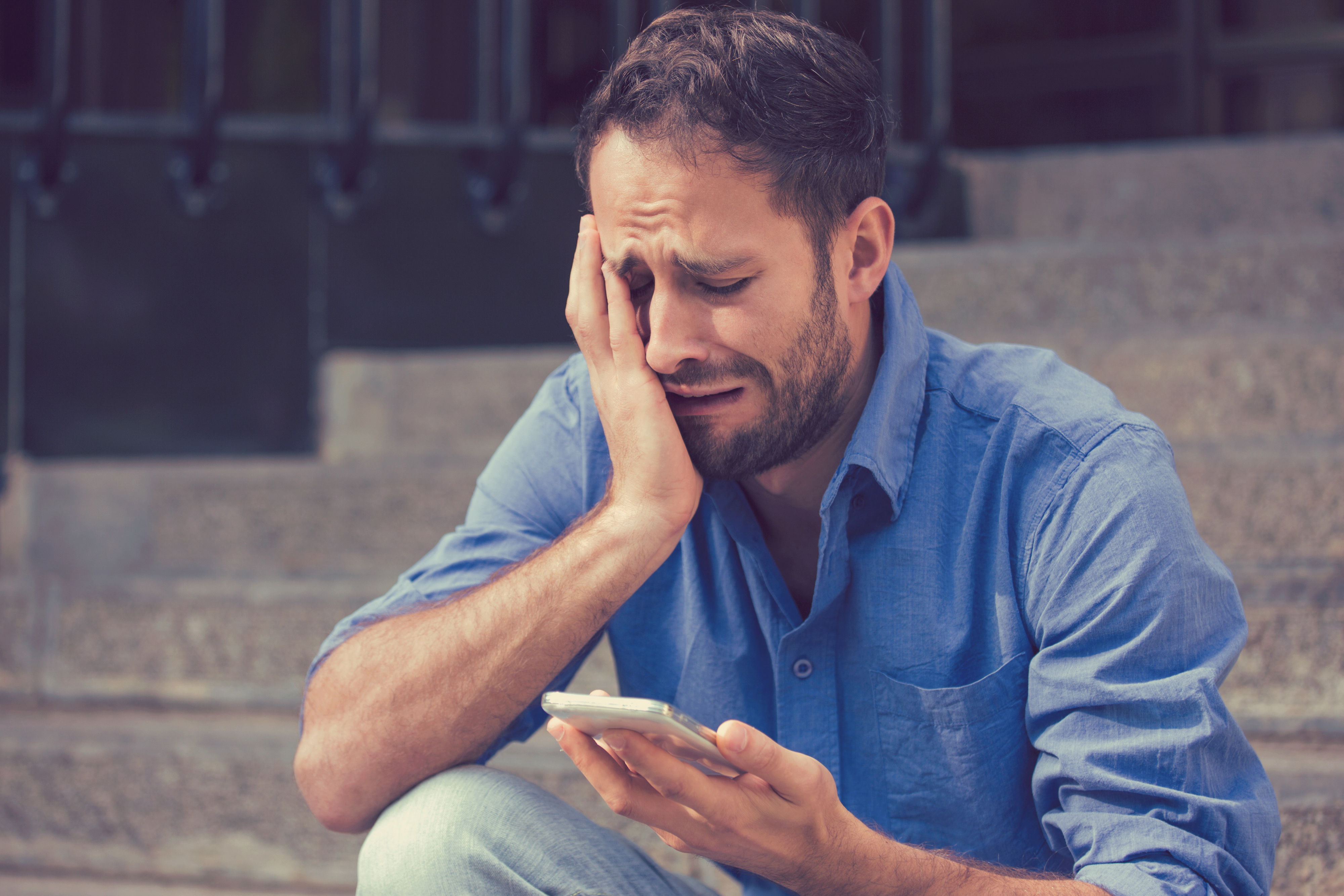 Weinender Mann, der auf sein Telefon schaut | Quelle: Shutterstock