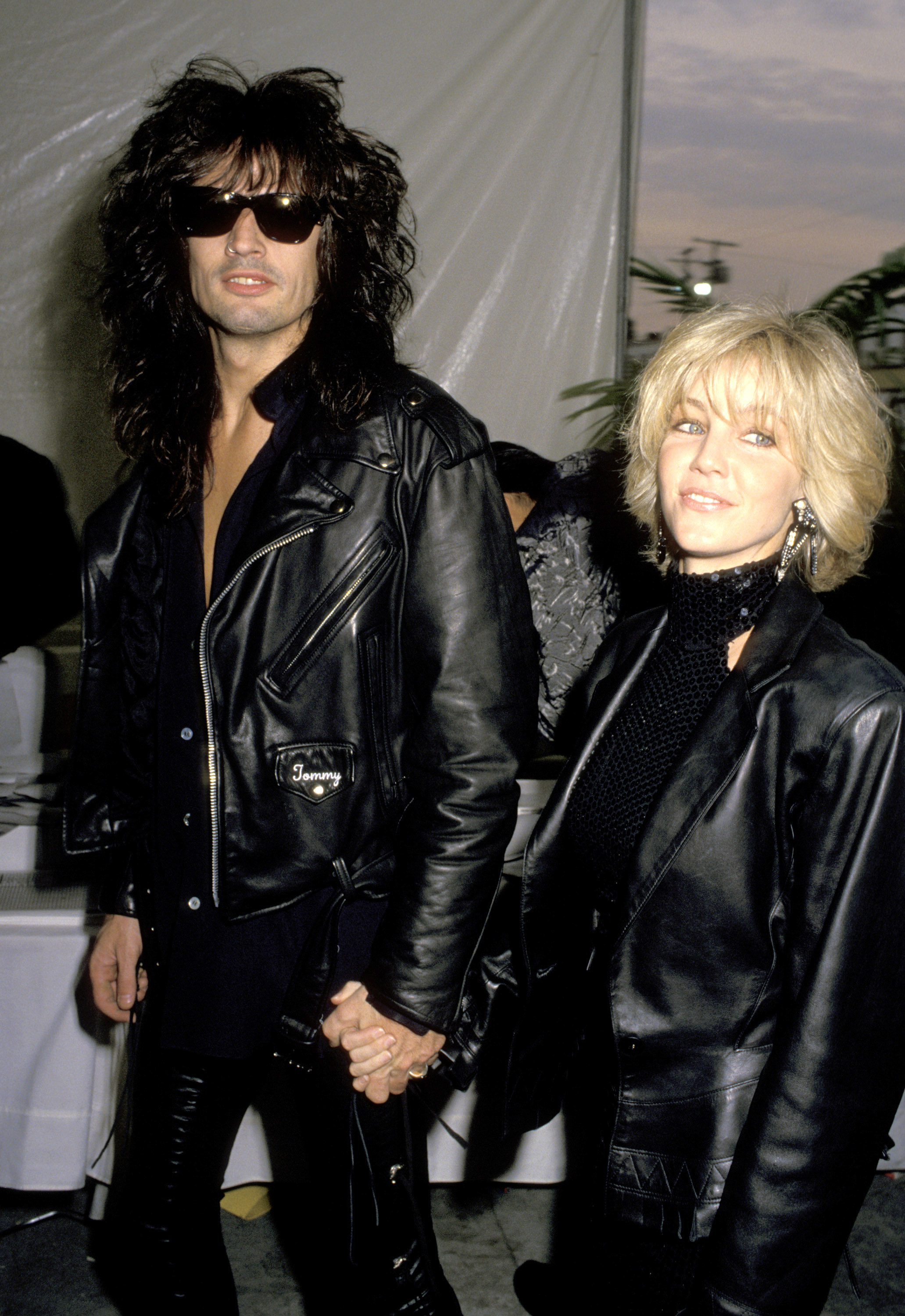 Heather Locklear und ihr damaliger Ehemann Tommy Lee sorgen am 21. Februar 1990 bei der 32. Grammy-Verleihung für einen auffälligen Auftritt, als sie Hand in Hand den Saal betreten. Das Rock-’n’-Roll-Powerpaar ist von Kopf bis Fuß in schwarzes Leder gekleidet: Lee trägt eine dunkle Sonnenbrille und eine bestickte Bikerjacke, während Locklear einen strukturierten blonden Bob, Hängeohrringe und ein hochgeschlossenes Pailletten-Top unter einem übergroßen Lederblazer präsentiert. | Quelle: Getty Images