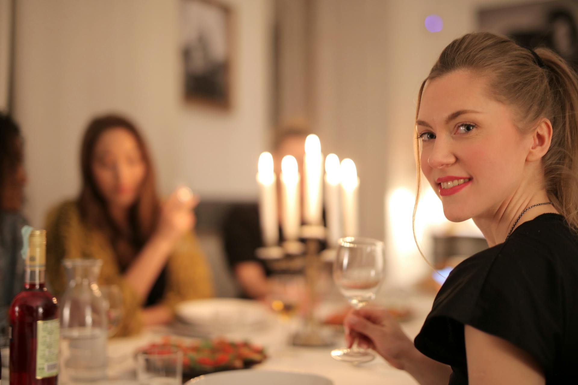 Eine Frau lächelt, während sie ein Glas Wein am Esstisch hält | Quelle: Pexels