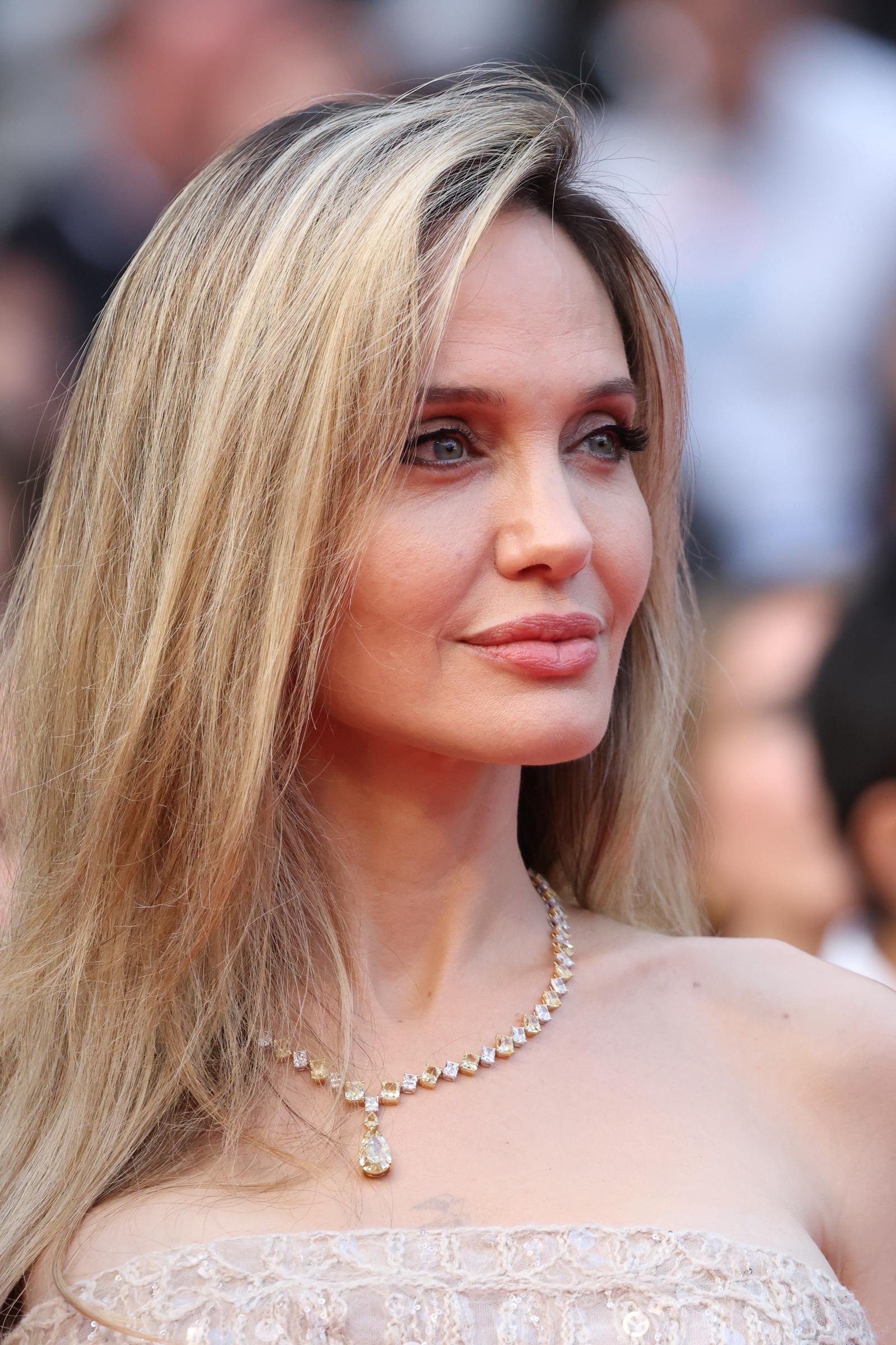 In einer Nahaufnahme, die jedes noch so kleine Detail einfängt, schimmern Angelina Jolies sanftes Glam-Make-up und ihre Diamantkette im Licht von Cannes und unterstreichen ihren gelassenen Ausdruck und ihre goldfarbene Eleganz.