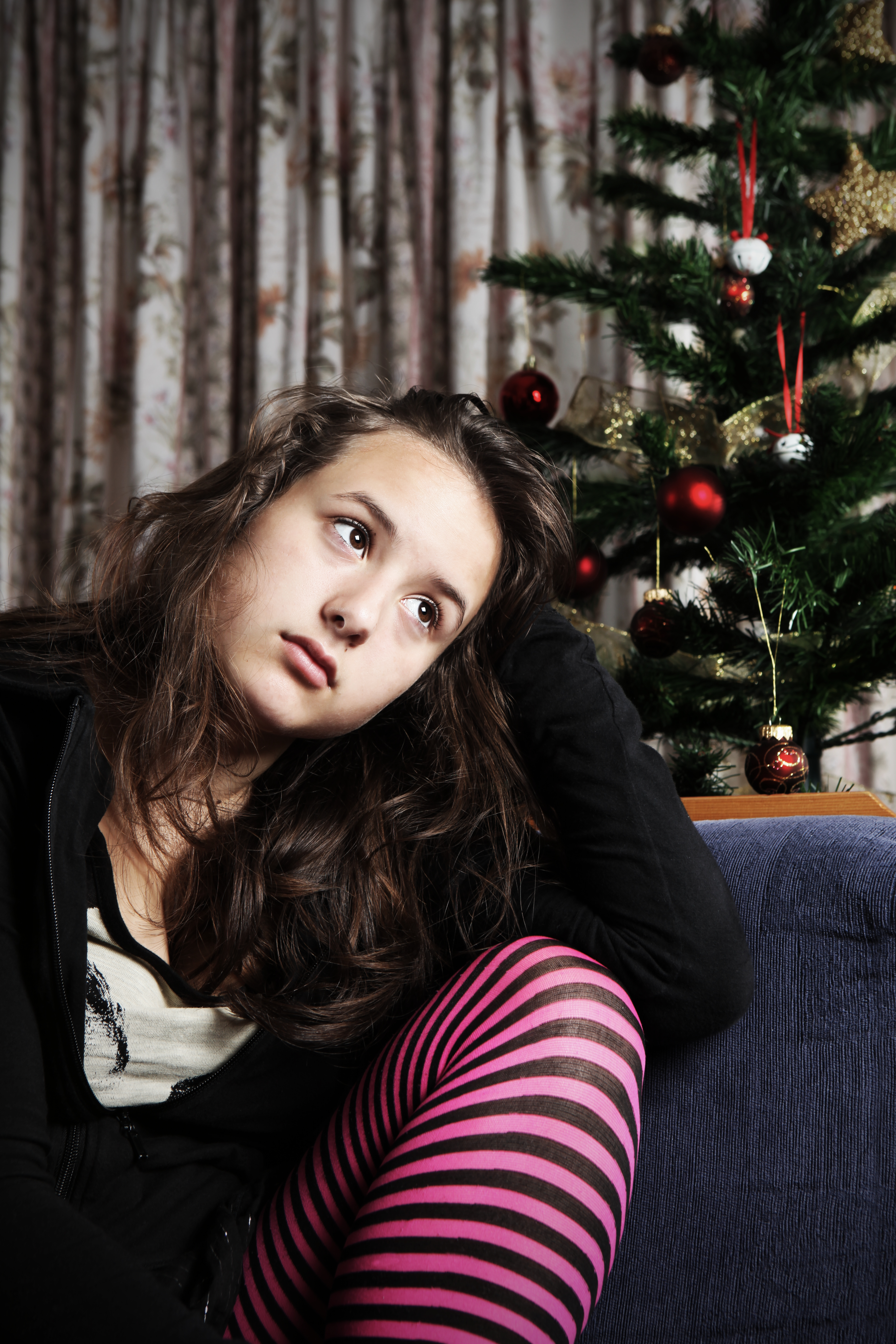 Ein trauriges Teenagermädchen sitzt neben einem Weihnachtsbaum | Quelle: Getty Images