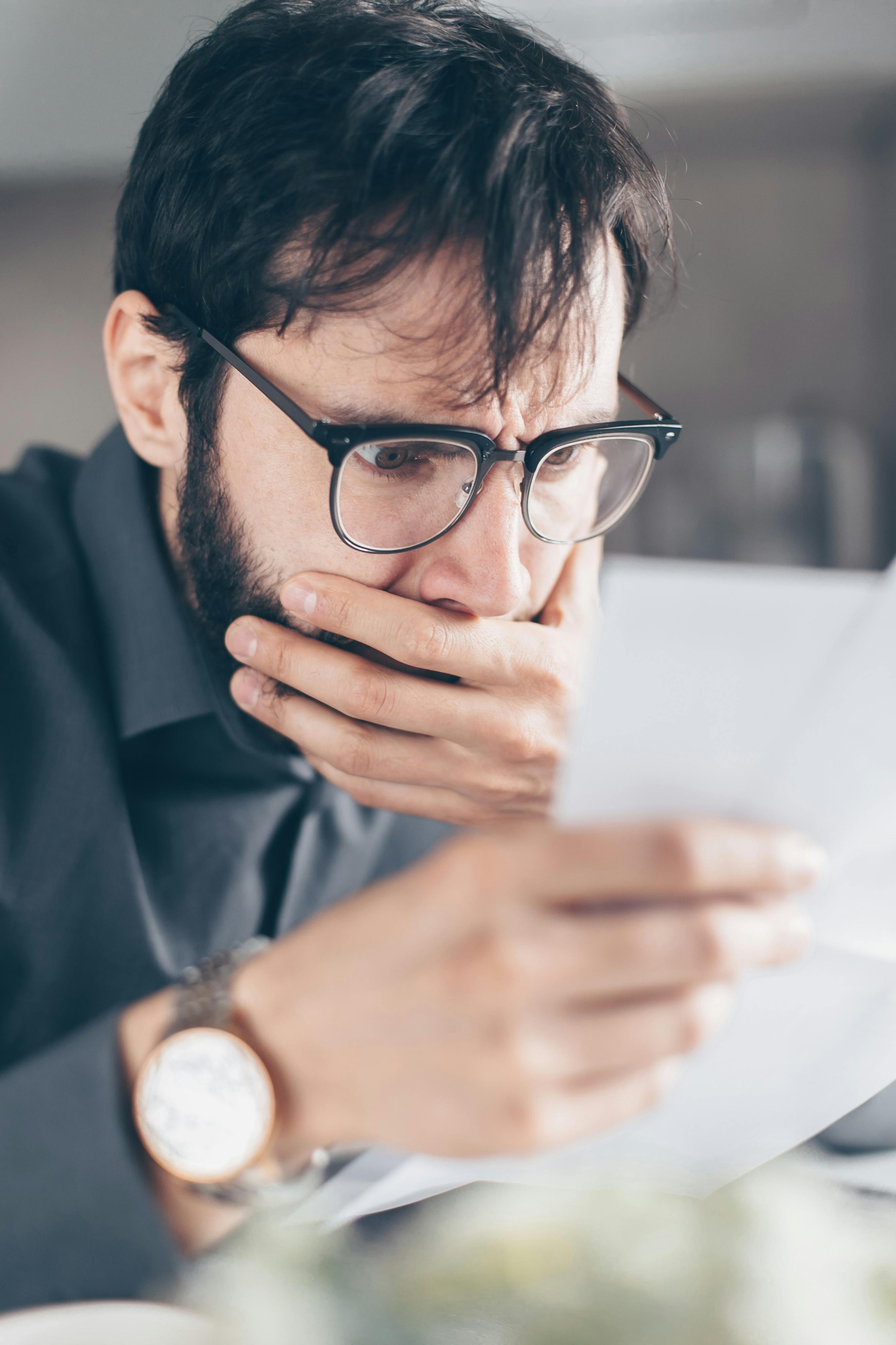 Ein schockierter Mann mit verdecktem Mund, der etwas auf einem Papier liest | Quelle: Pexels