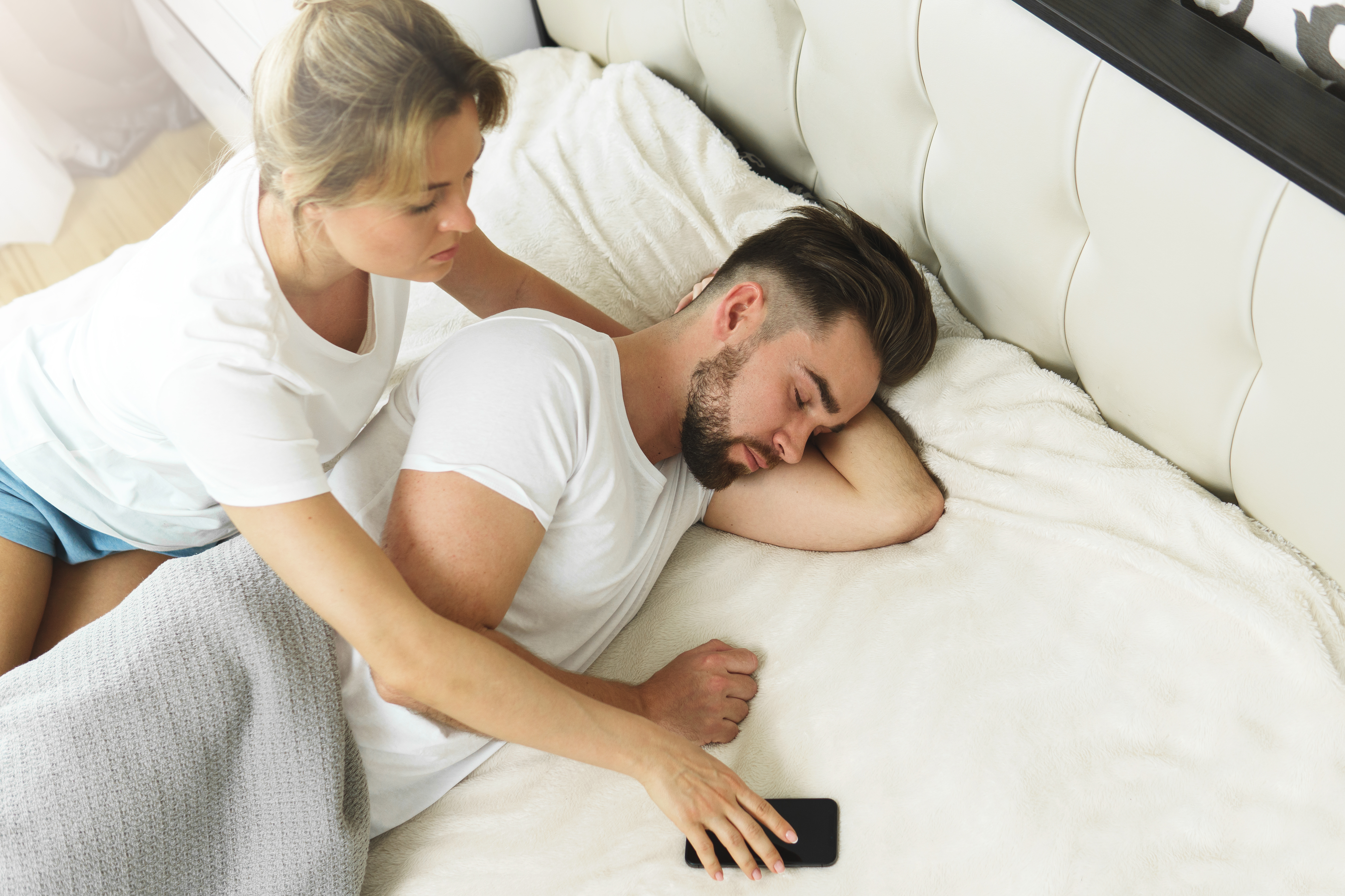 Eine Frau, die versucht, ihrem Partner das Telefon wegzunehmen, während er schläft | Quelle: Shutterstock