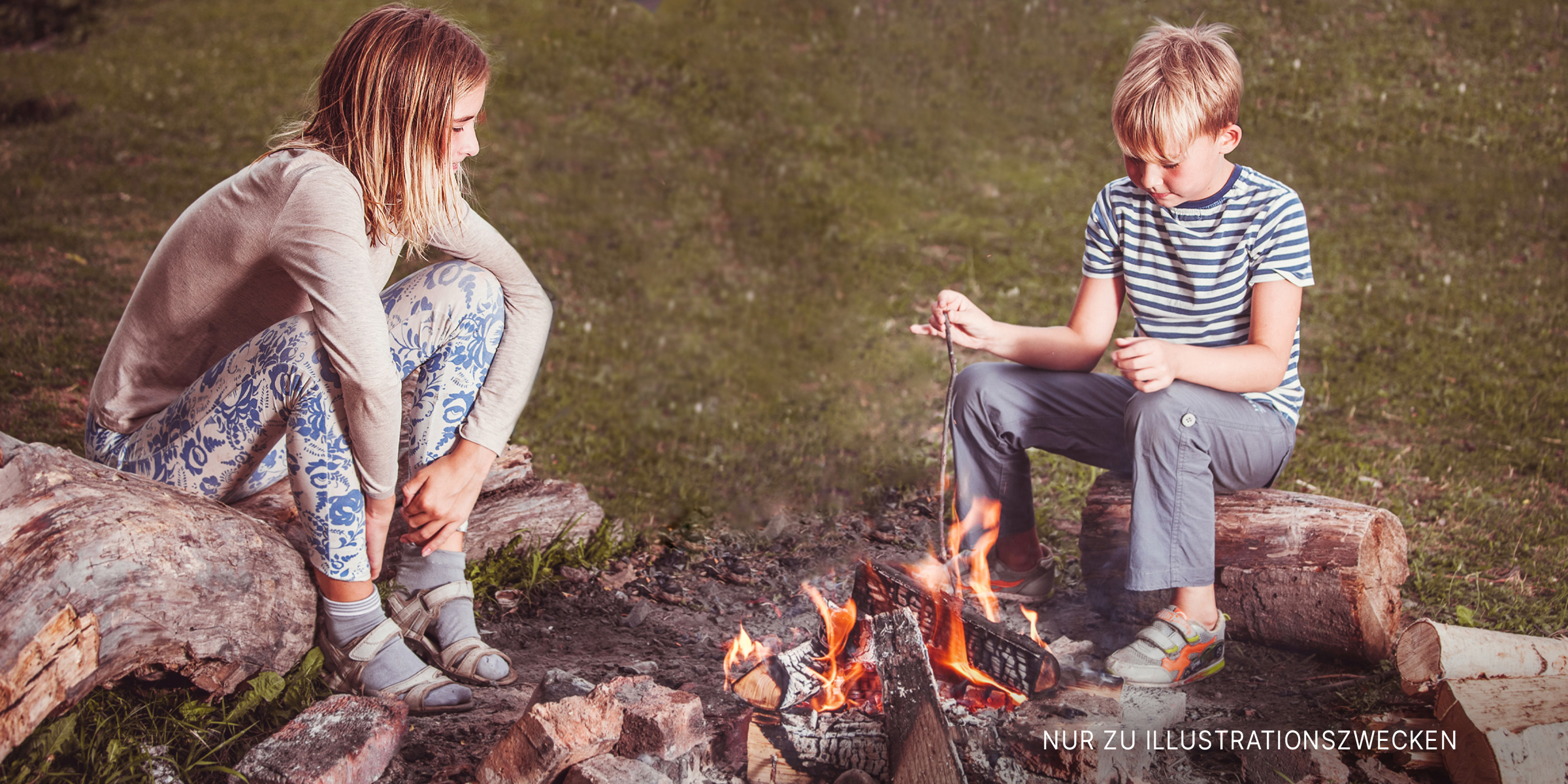 Ein Junge und ein Mädchen sitzen sich an einem Lagerfeuer gegenüber | Quelle: Shutterstock