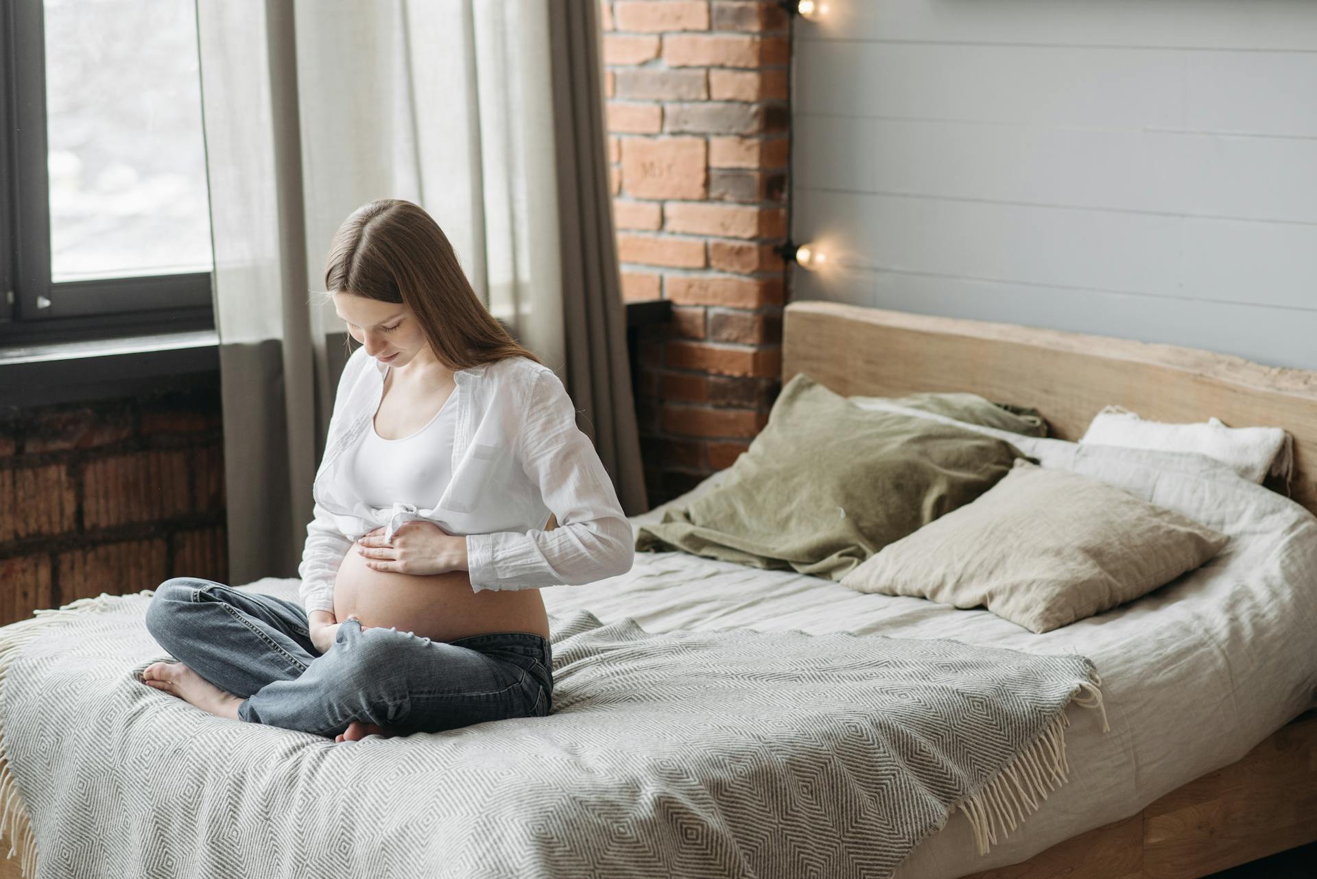 Eine schwangere Frau, die auf dem Bett sitzt und ihren Bauch hält | Quelle: Pexels