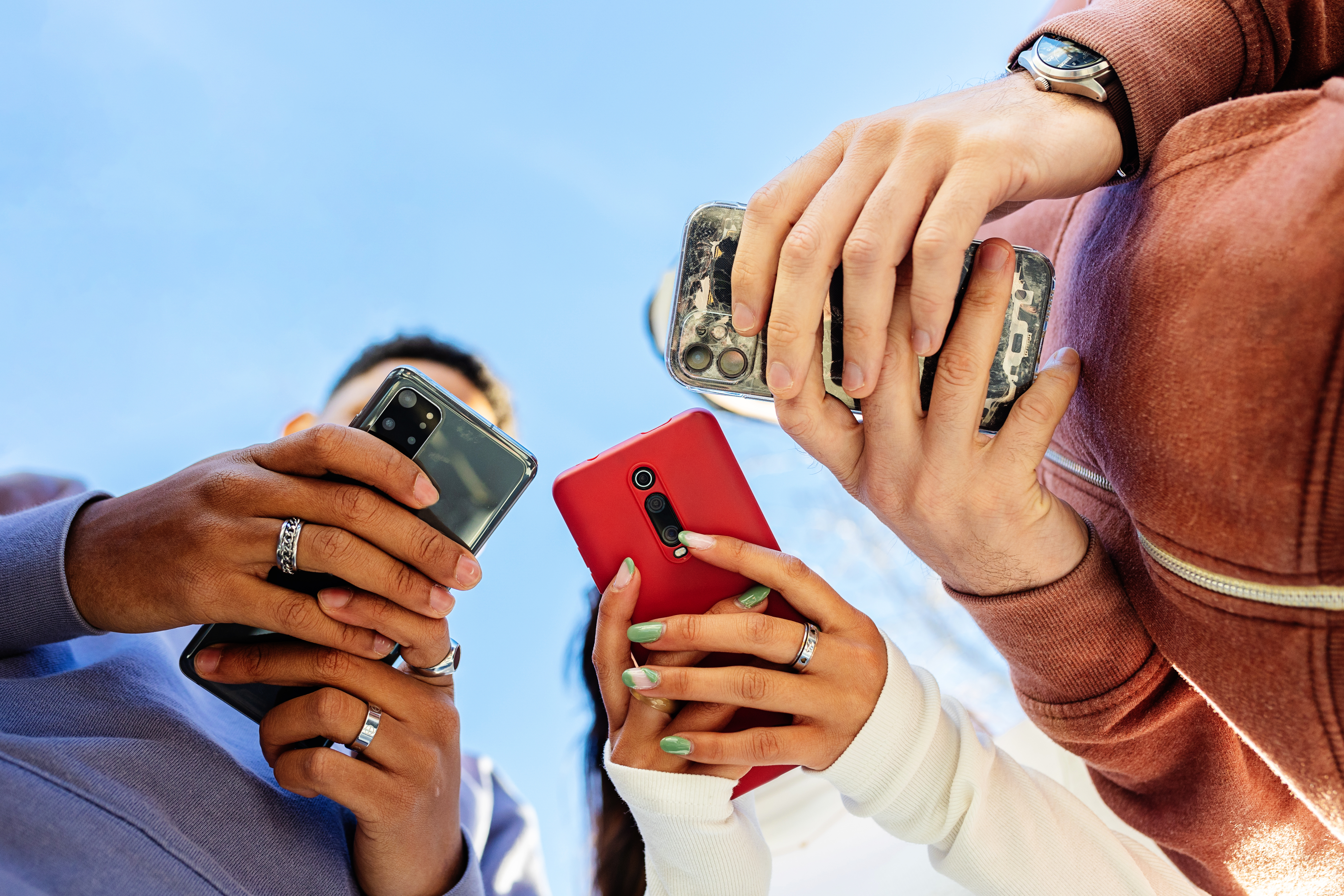 Tiefblick auf drei junge Menschen, die im Freien mit dem Handy telefonieren | Quelle: Getty Images