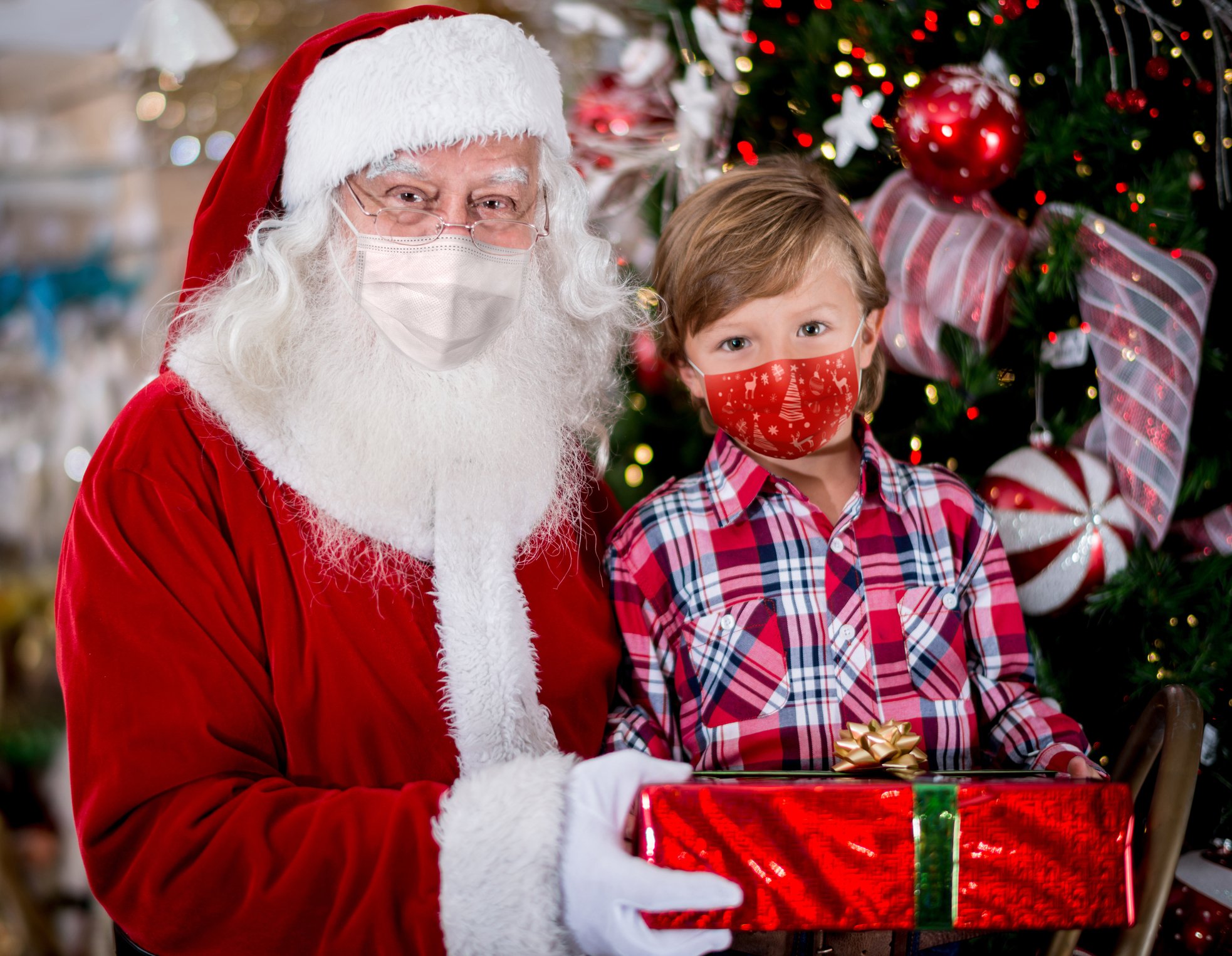 Porträt eines kleinen Jungen mit dem Weihnachtsmann, der Gesichtsmasken trägt, während er ein Geschenk erhält. | Quelle: Getty Images