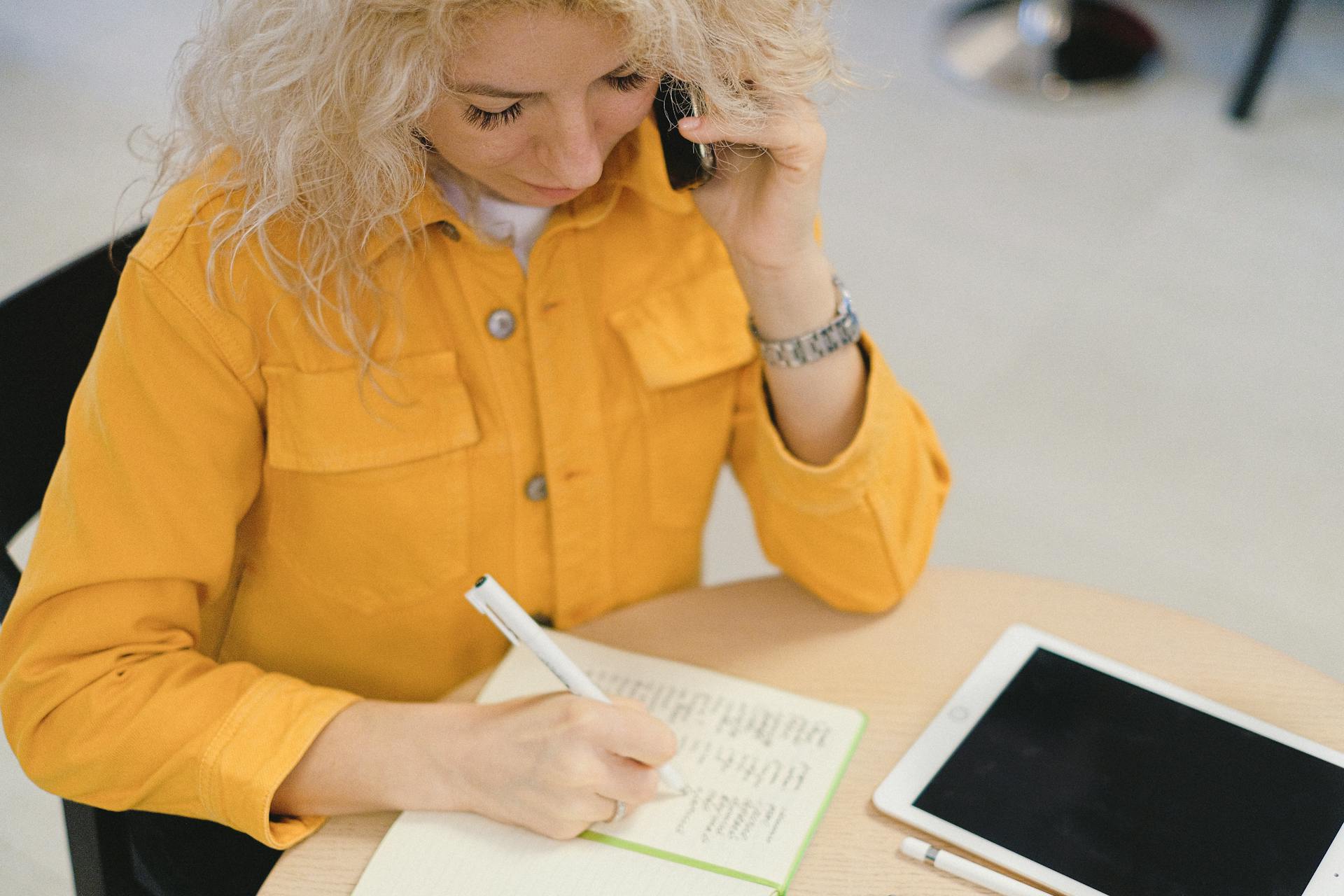 Eine Frau, die in ihr Notizbuch schreibt, während sie telefoniert | Quelle: Pexels