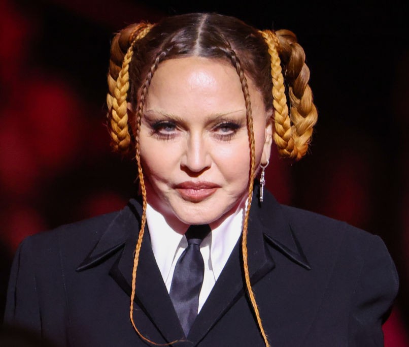 Madonna blickt in die Kamera – in einem schwarzen, maßgeschneiderten Anzug, einem weißen Hemd und einer schwarzen Krawatte, mit aufwendig geflochtenen Locken und langen Zöpfen, die ihr Gesicht umrahmen. | Quelle: Chat GPT