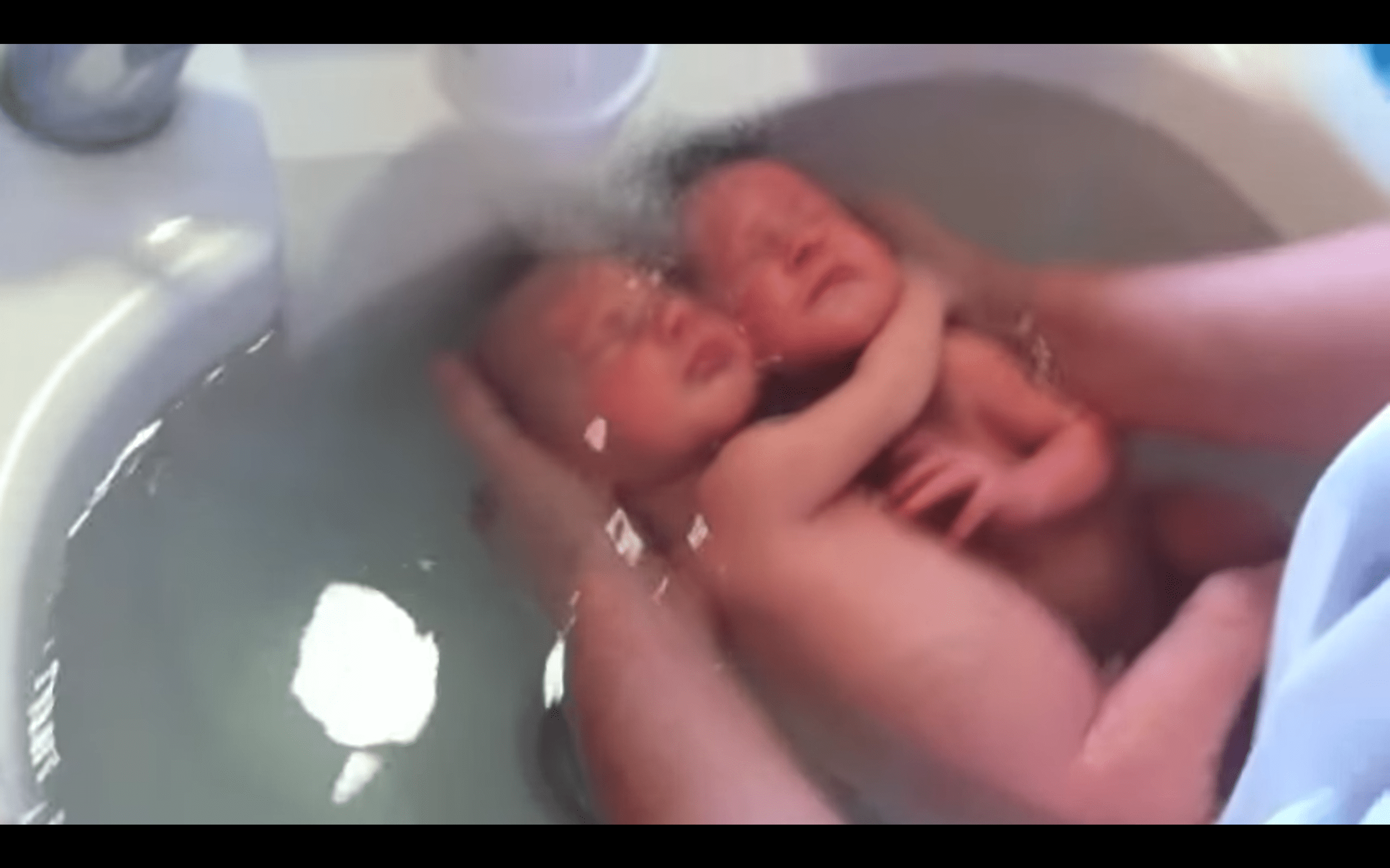 Zwillingsbabys, die sich in einem Video, das eine Krankenschwester beim Baden der beiden geteilt hat, aneinander festhalten. | Quelle: Youtube.com/massagebebe
