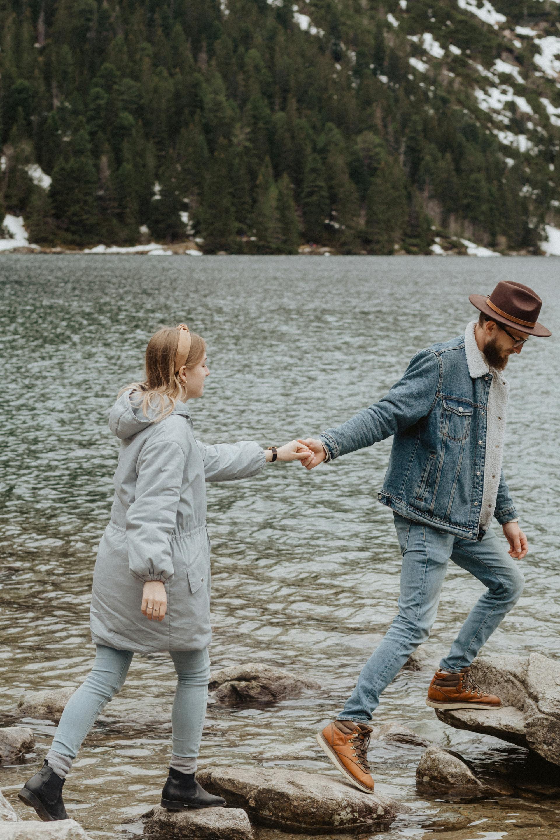 Ein Paar spaziert auf Felsen in der Nähe eines Sees | Quelle: Pexels